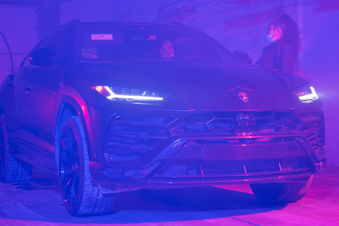 Matte black Lamborghini Urus SUV displayed under purple atmospheric lighting at event.