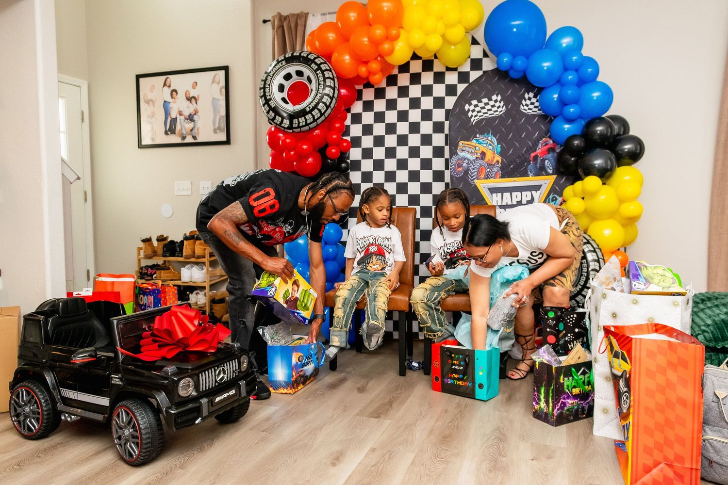 Adults and children opening birthday gifts at a race car themed party with colorful balloon arch.