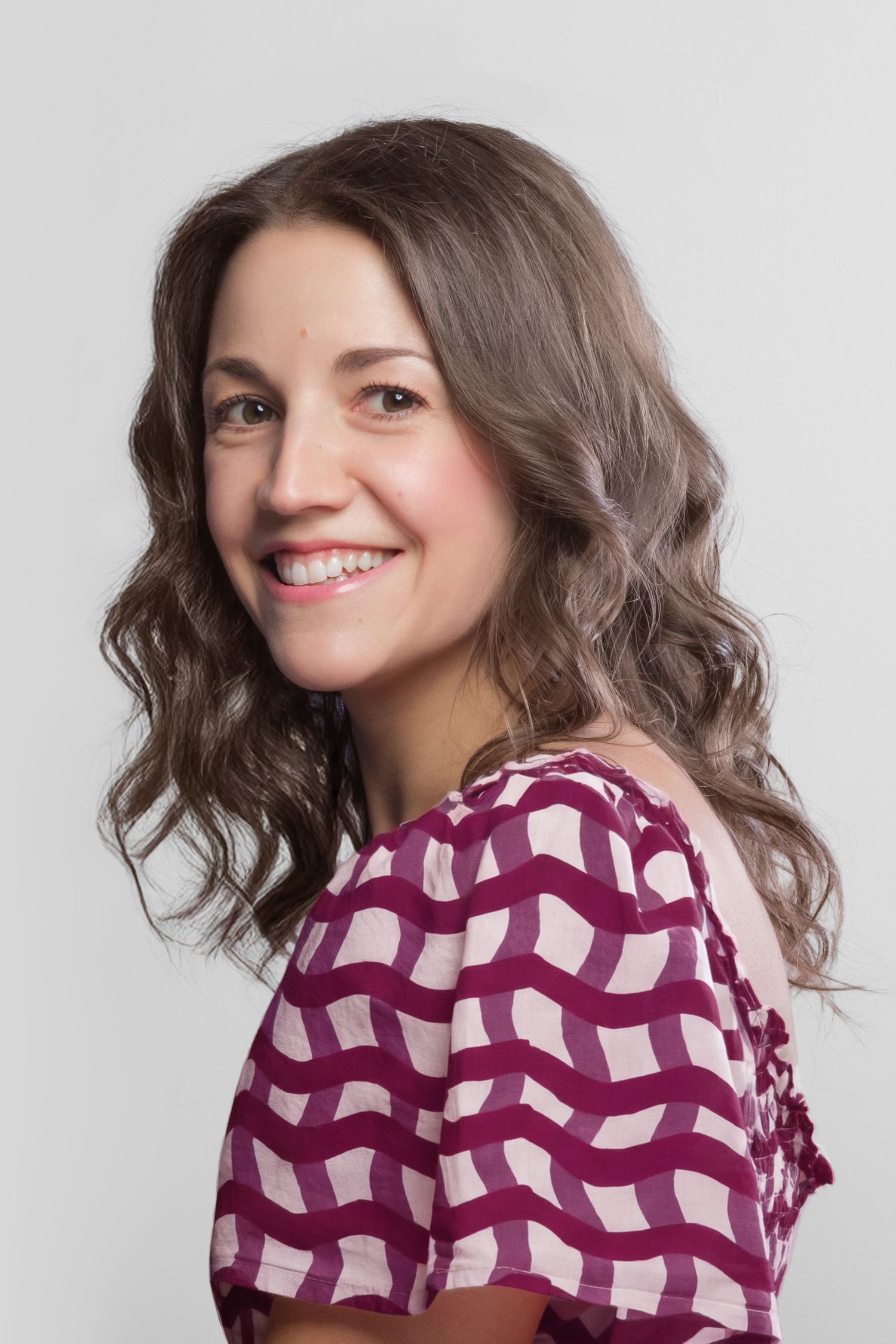 Darina Todorova, smiling at the camera with wavy brown hair wearing a purple patterned dress against a light gray background.
