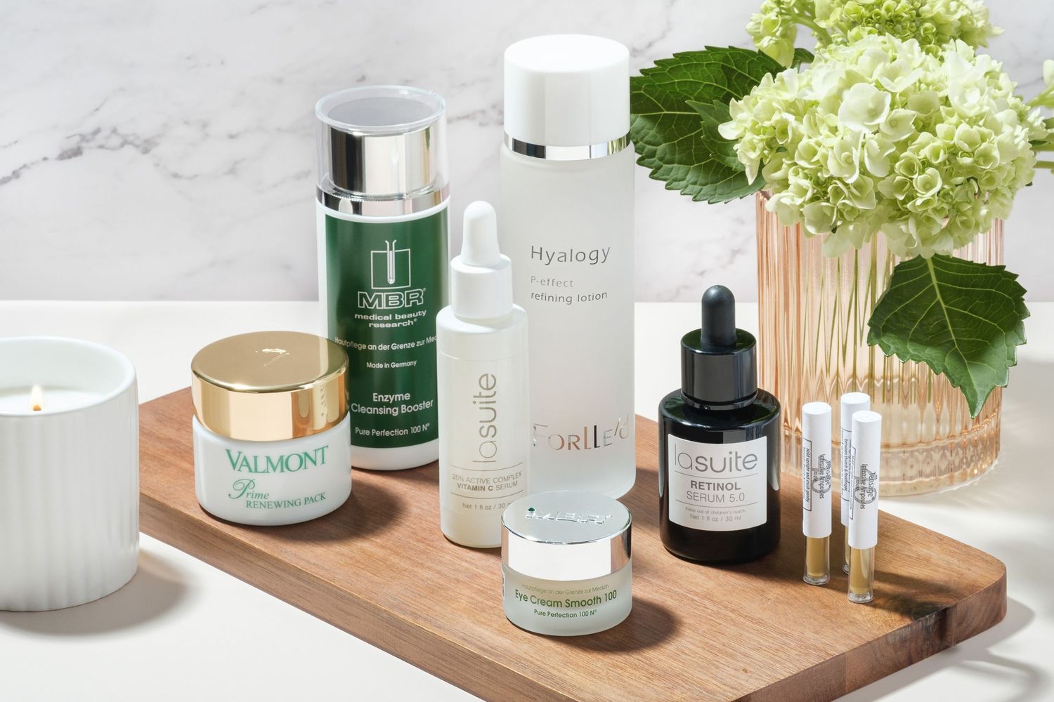 Luxury skincare products arranged on a wooden tray, featuring Valmont, Hyalogy, MBR, La Suite and other premium serums and creams.