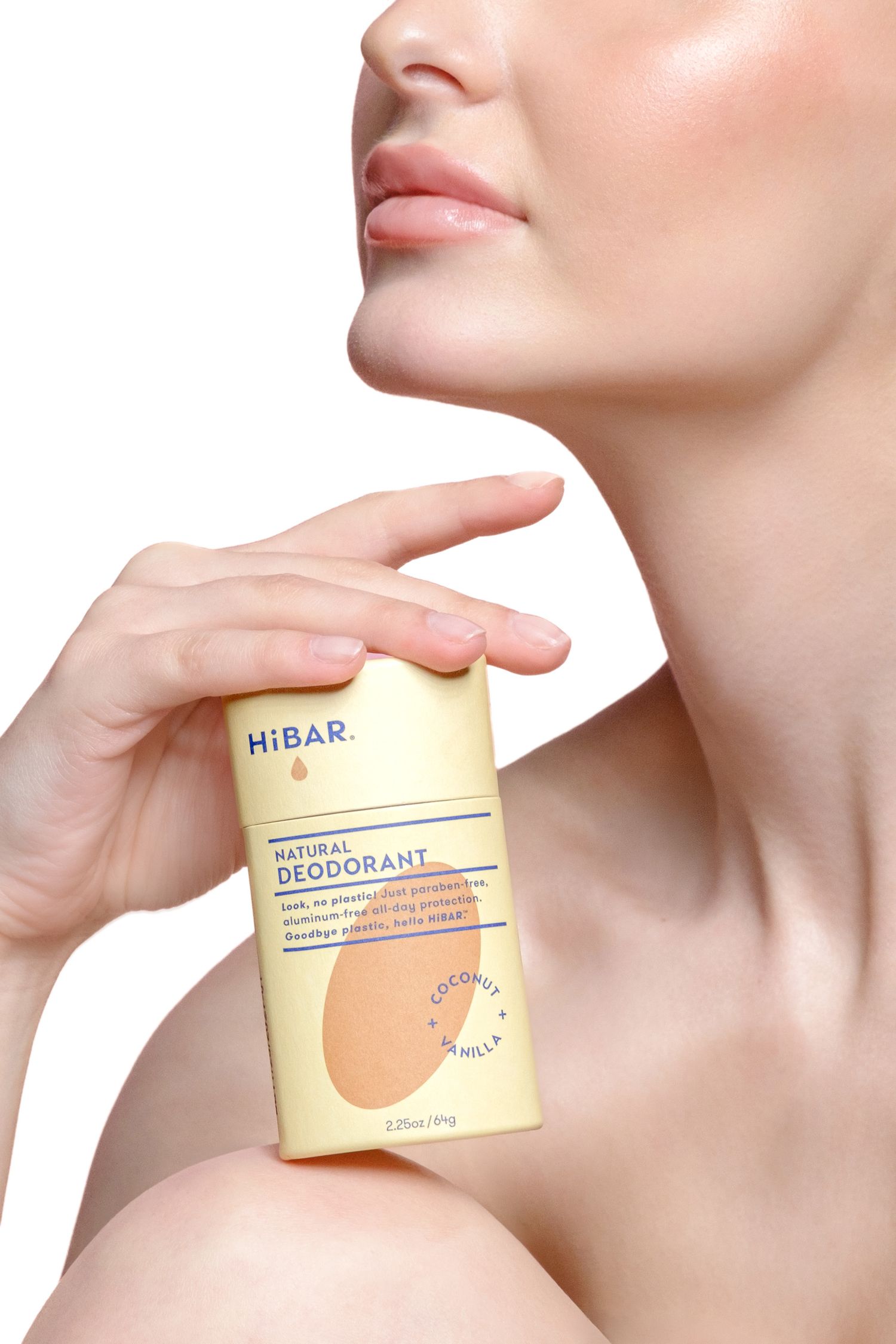 A woman holding HiBAR natural deodorant stick in coconut vanilla scent over her leg on a white background. Professional studio photo.