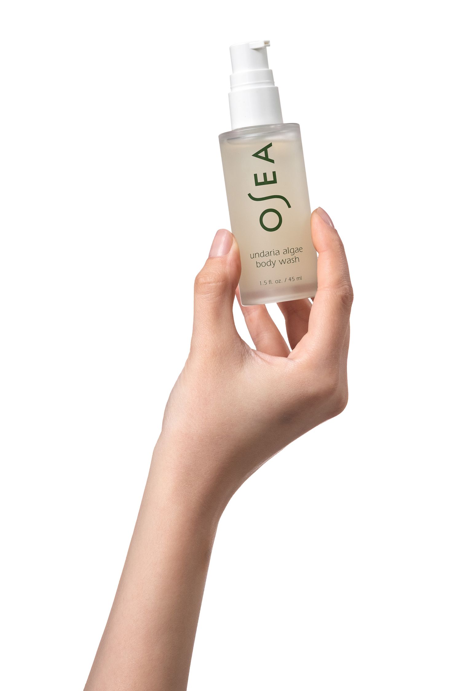 A hand holding a clear pump bottle of OSEA undaria algae body wash against a light grey background. Professional studio photo.