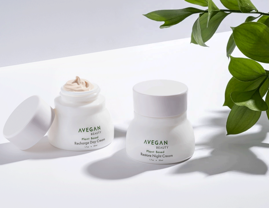 A Vegan Beauty day and night cream jars, arranged with gently moving greenery leaves against light background with bright sunny light.