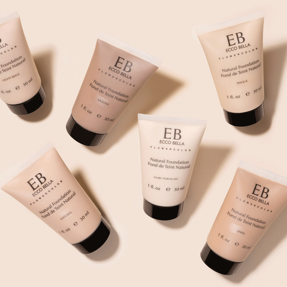 Ecco Bella foundation makeup tubes captured appearing and disappearing overhead on a light beige background.