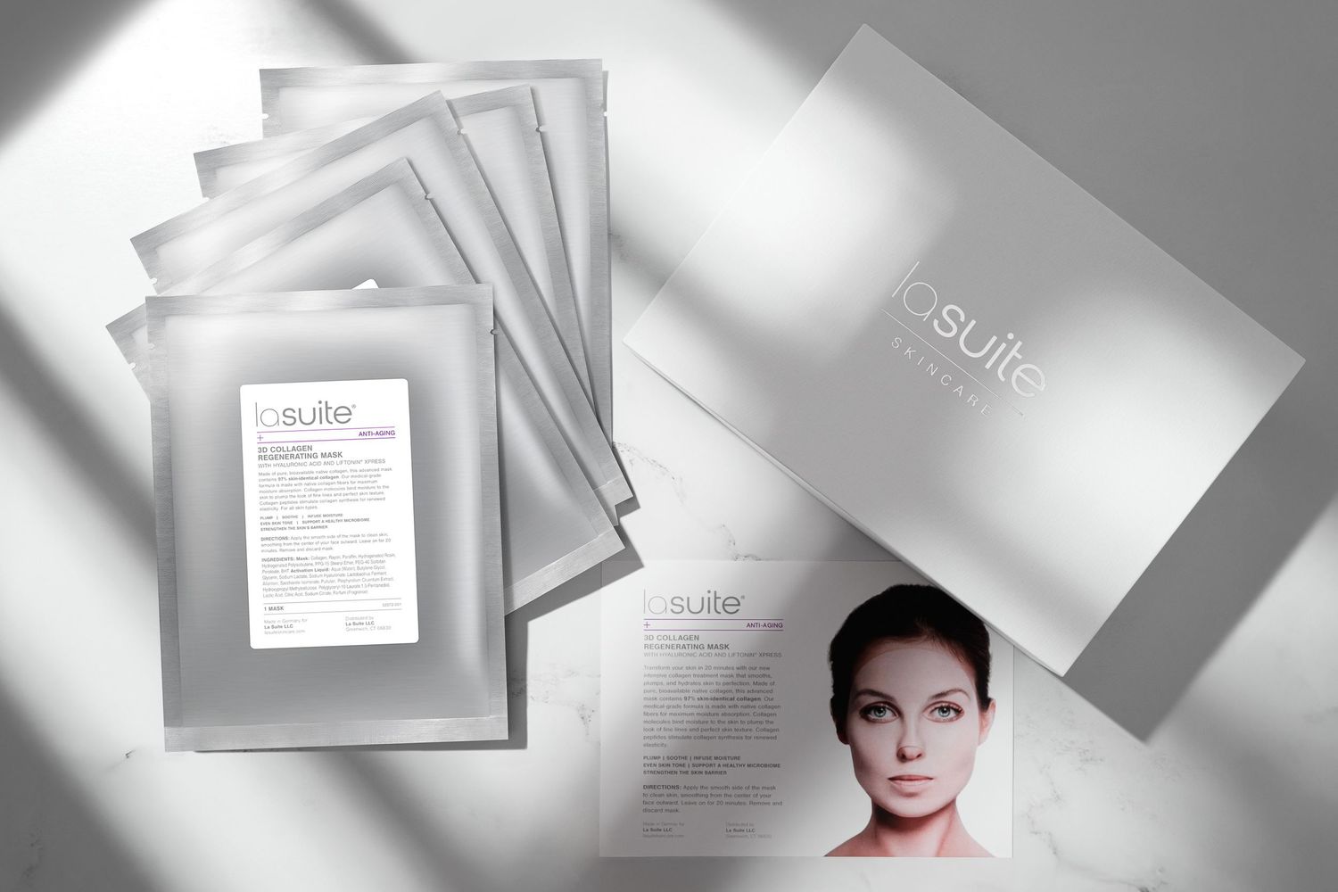 La Suite skincare face masks displayed with product packaging and a card with woman's portrait on a marble countertop with bright sun light.