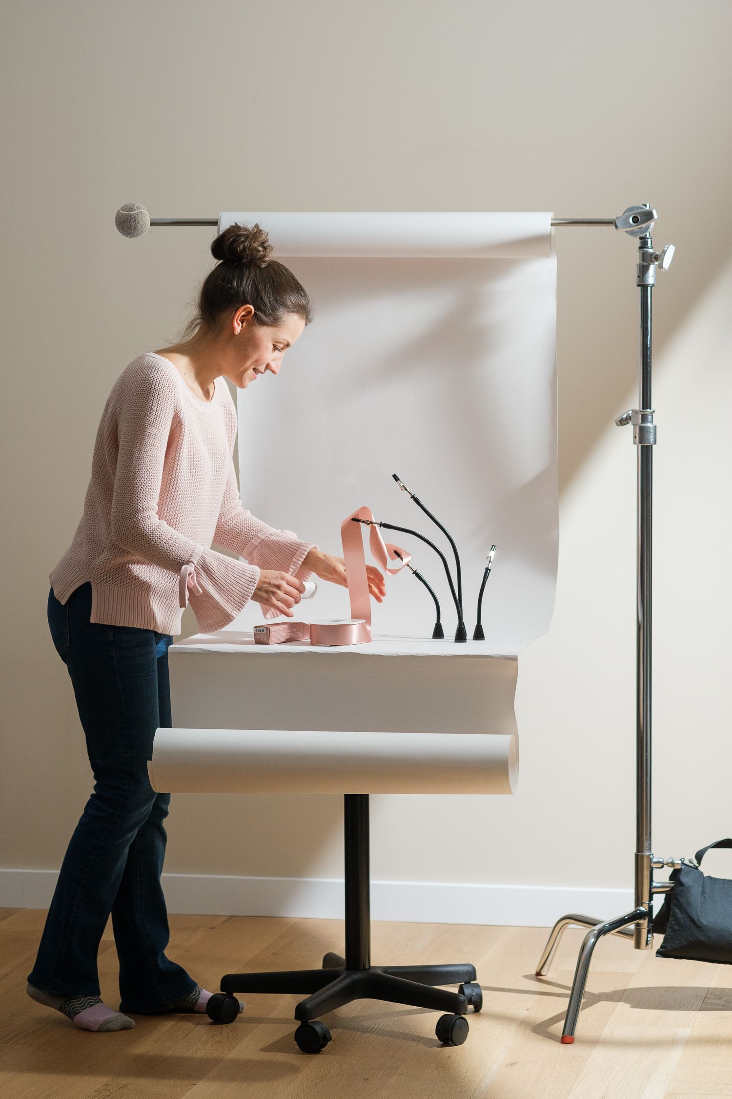 Darina arranging pink ribbon with magnetic helping hands in her home photo studio with white backdrop and a bright sun light.
