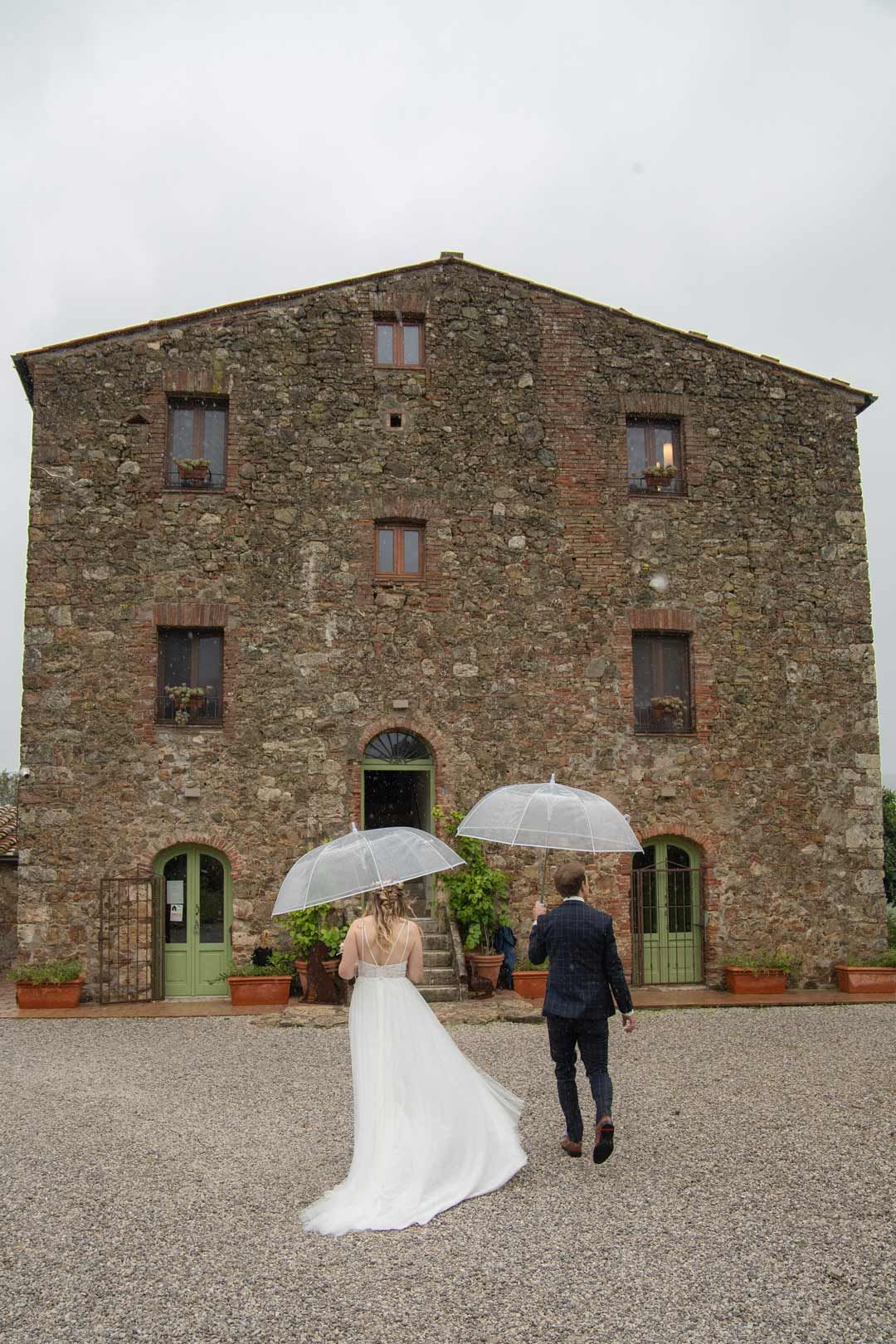 Hochzeitsfotografie: Hochzeitspaar läuft mit Schirm auf das Haus zu