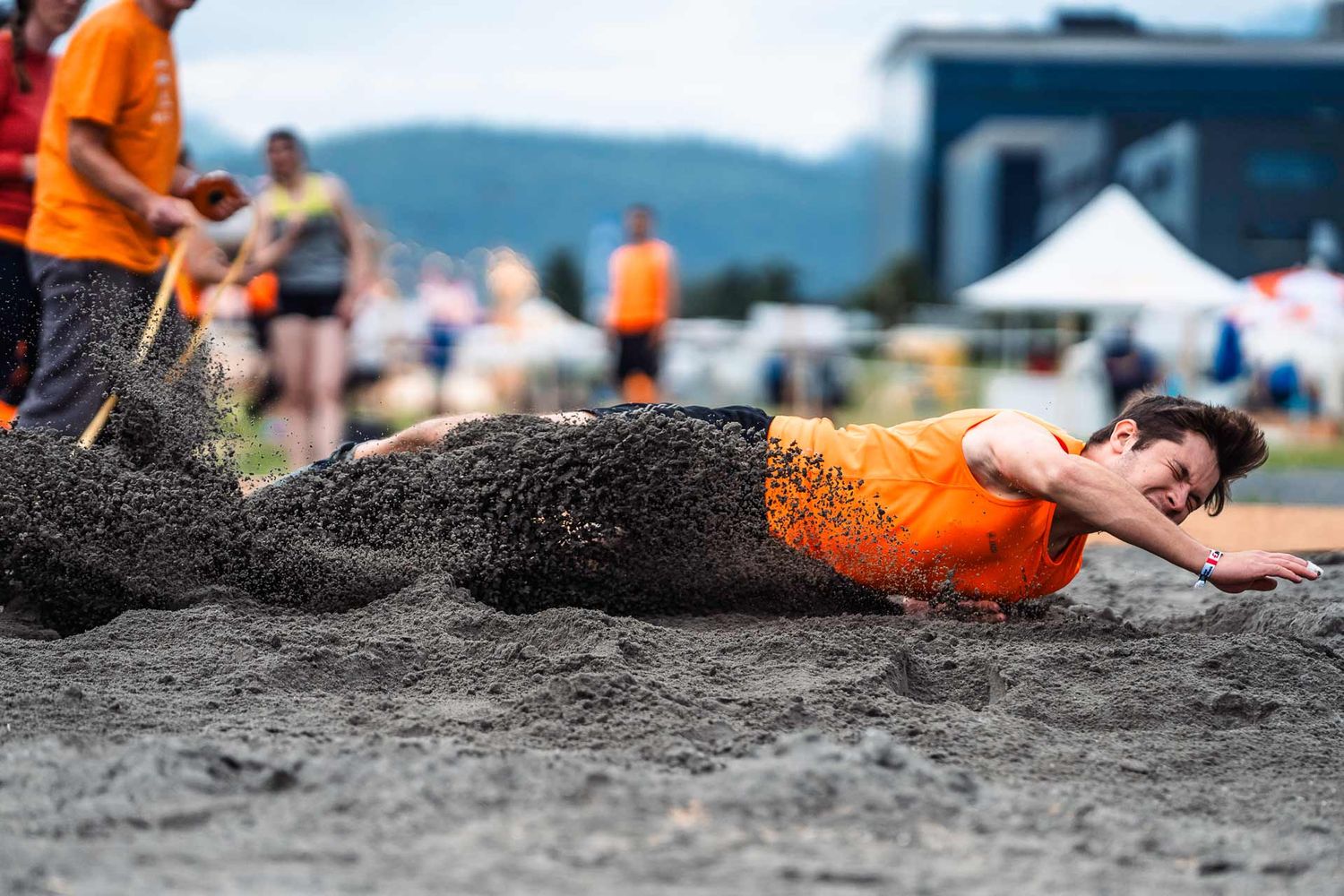 Eventfotografie: Leichtathlet springt in den Sand. Der Sand fliegt durch die Luft