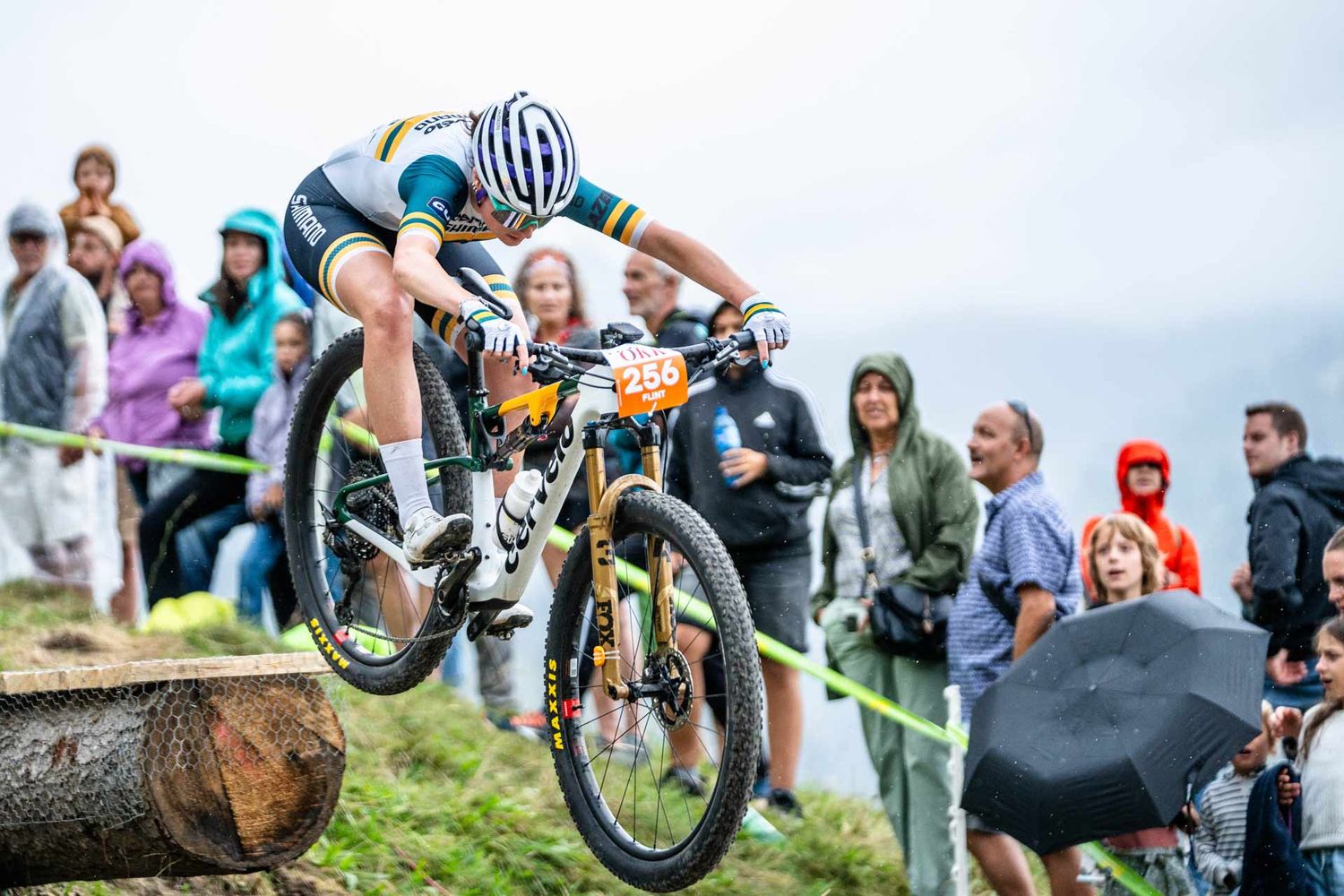 Eventfotografie: Mountainbikerin springt über einen Drop. Zuschauer feuern sie an