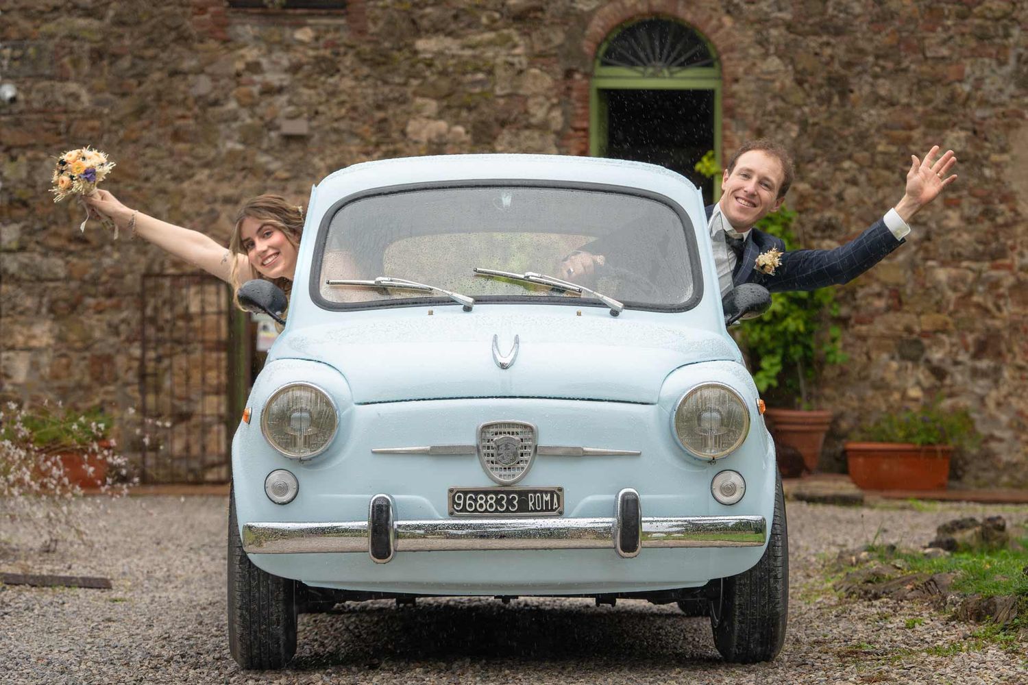 Hochzeitsfotografie: Hochzeitspaar schaut aus einem Oldtimer raus und jubelt