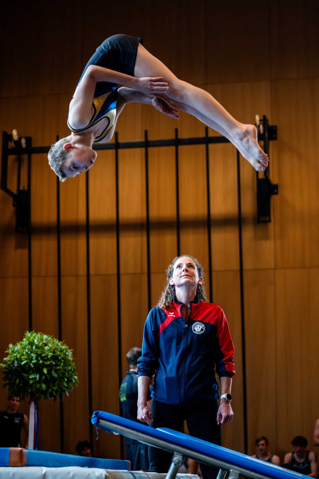 Sportfotografie: Junge macht Salto – seine Trainerin beobachtet ihn
