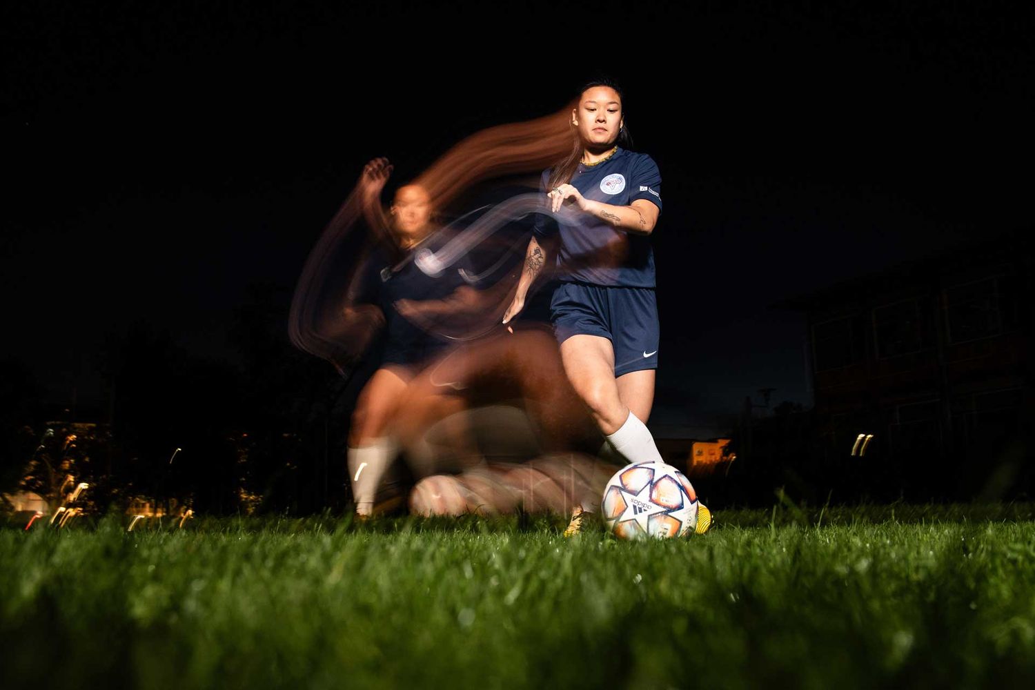 Fussballerin in dribbelt mit Ball - umgesetzt mit kreativem Blitz und Langzeitbelichtung für Lichteffekte