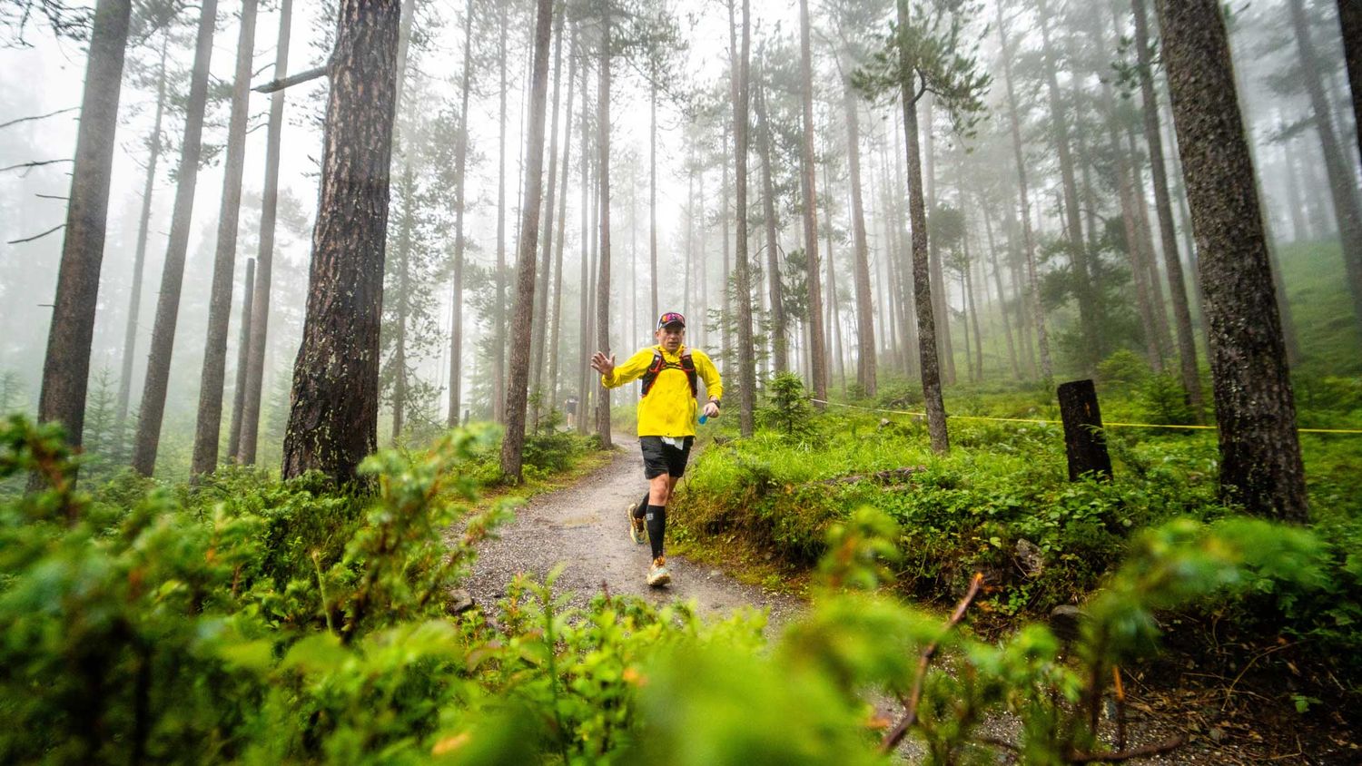 Eventfotografie: Läufer läuft durch den Wald und winkt in die Kamera
