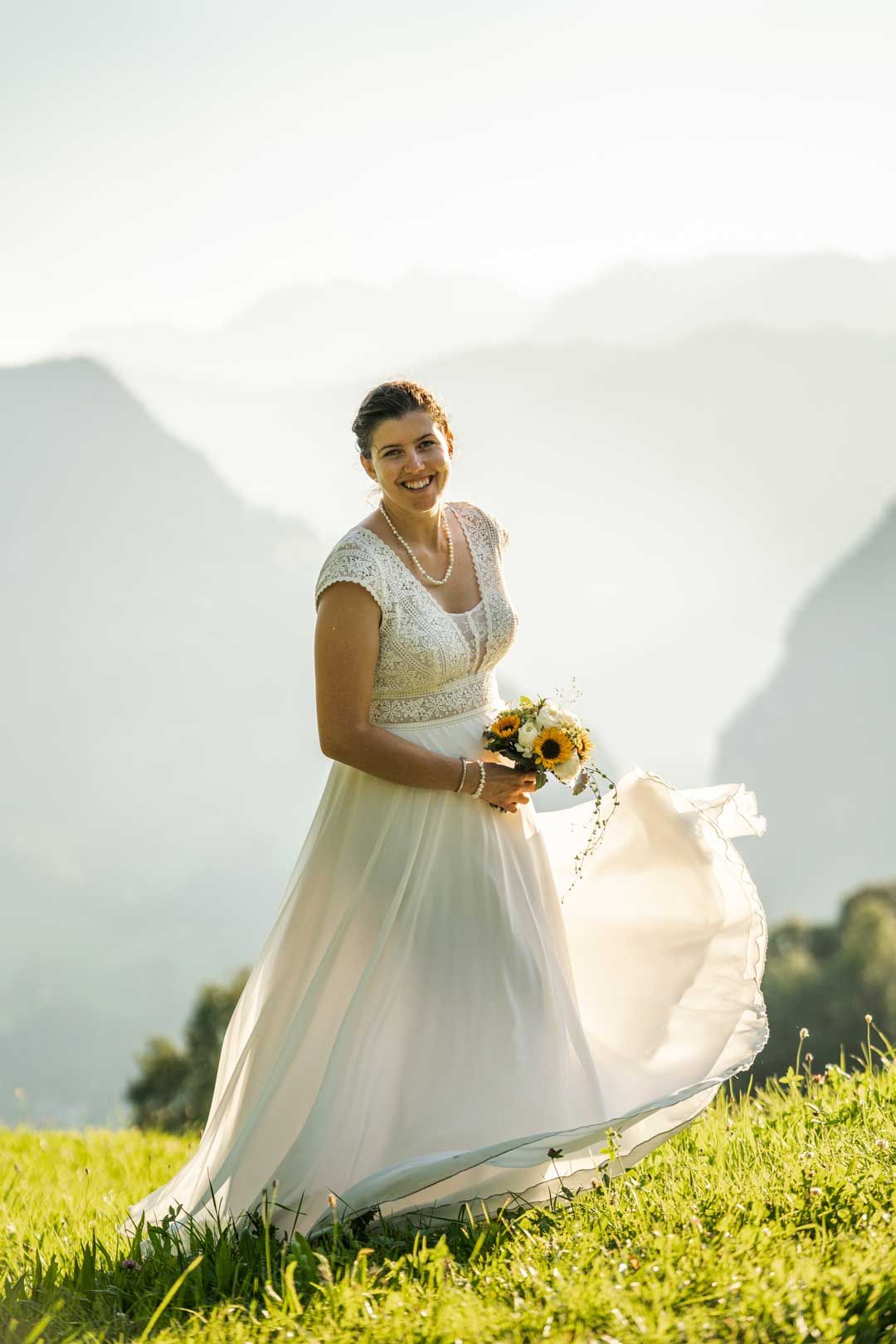 Hochzeitsfotografie: Braut geniesst die Sonne auf einer Wiese – Ihr Hochzeitskleid weht im Wind