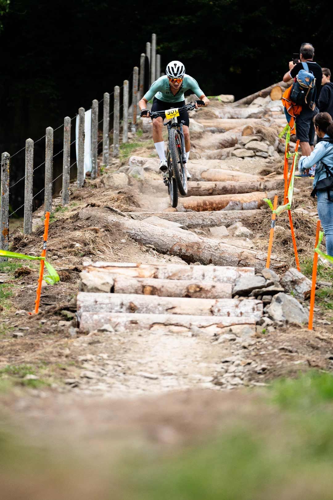 Eventfotografie: Mountainbiker springt über eine technische Passage. Zuschauer feuern ihn an