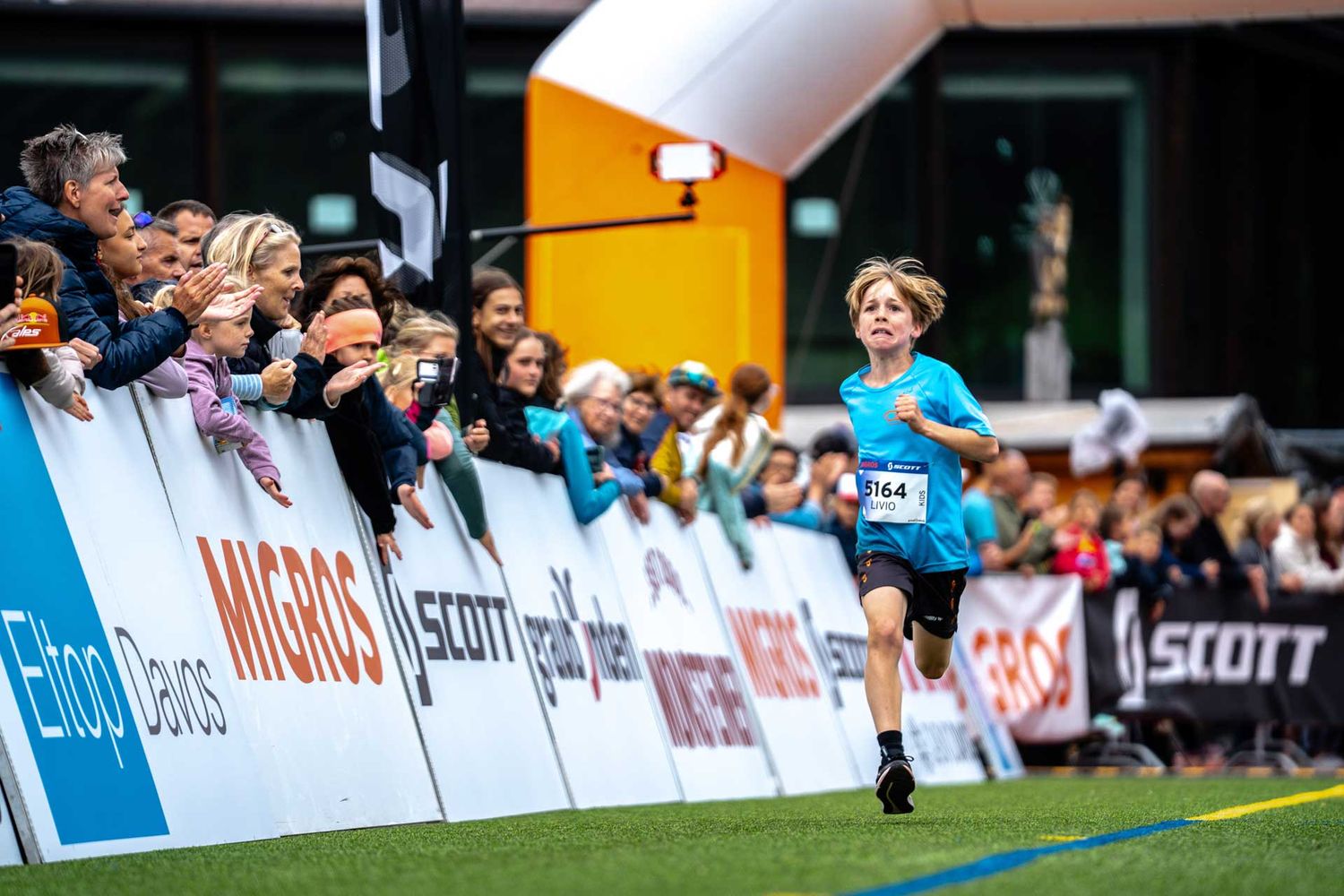 Eventfotografie: Junge sprintet locker ins Ziel – Zuschauer feuern ihn an