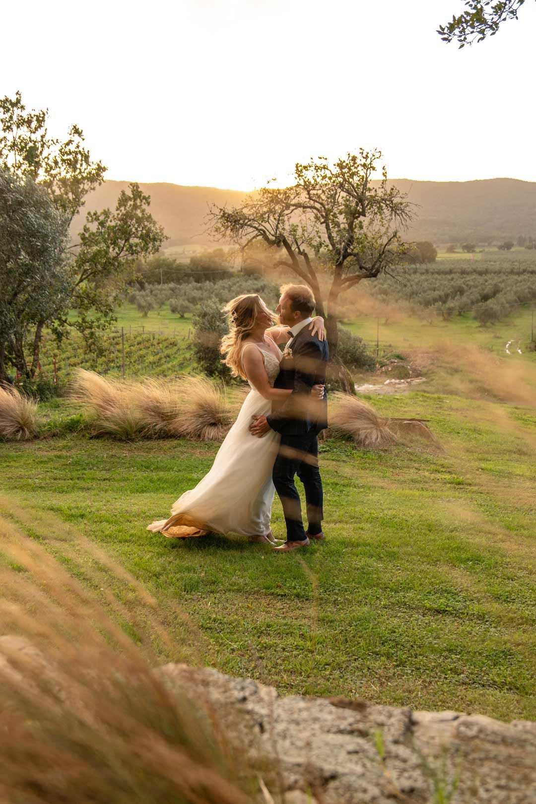 Hochzeitsfotografie: Das Hochzeitspaar tanzt im Sonnenuntergang. Romantische Stimmung mit goldenen Gräsern und tiefer Sonne