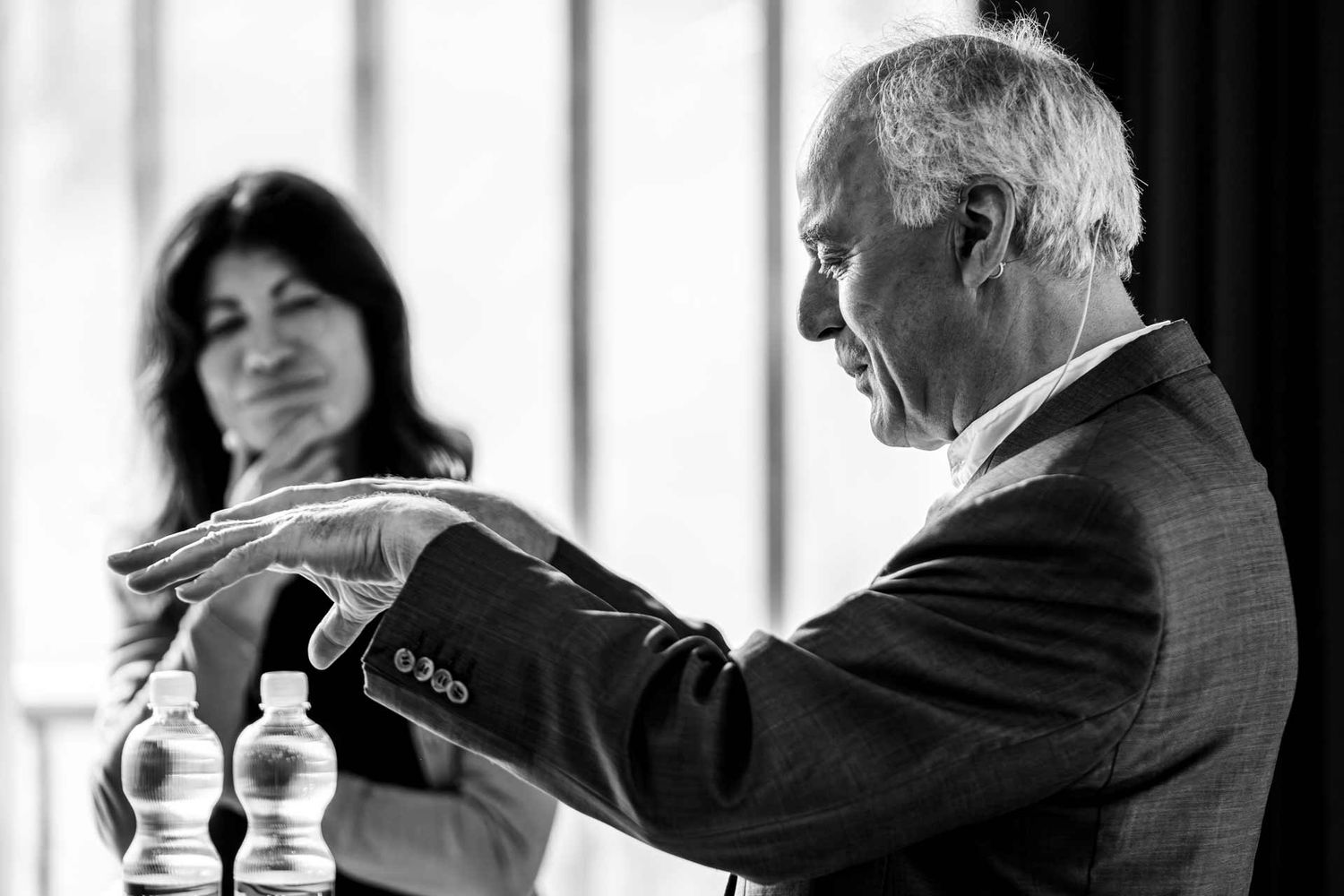 Eventfotografie: Redner auf der Bühne beim Alps Forum im Hintergrund hört Moderatorin gespannt zu