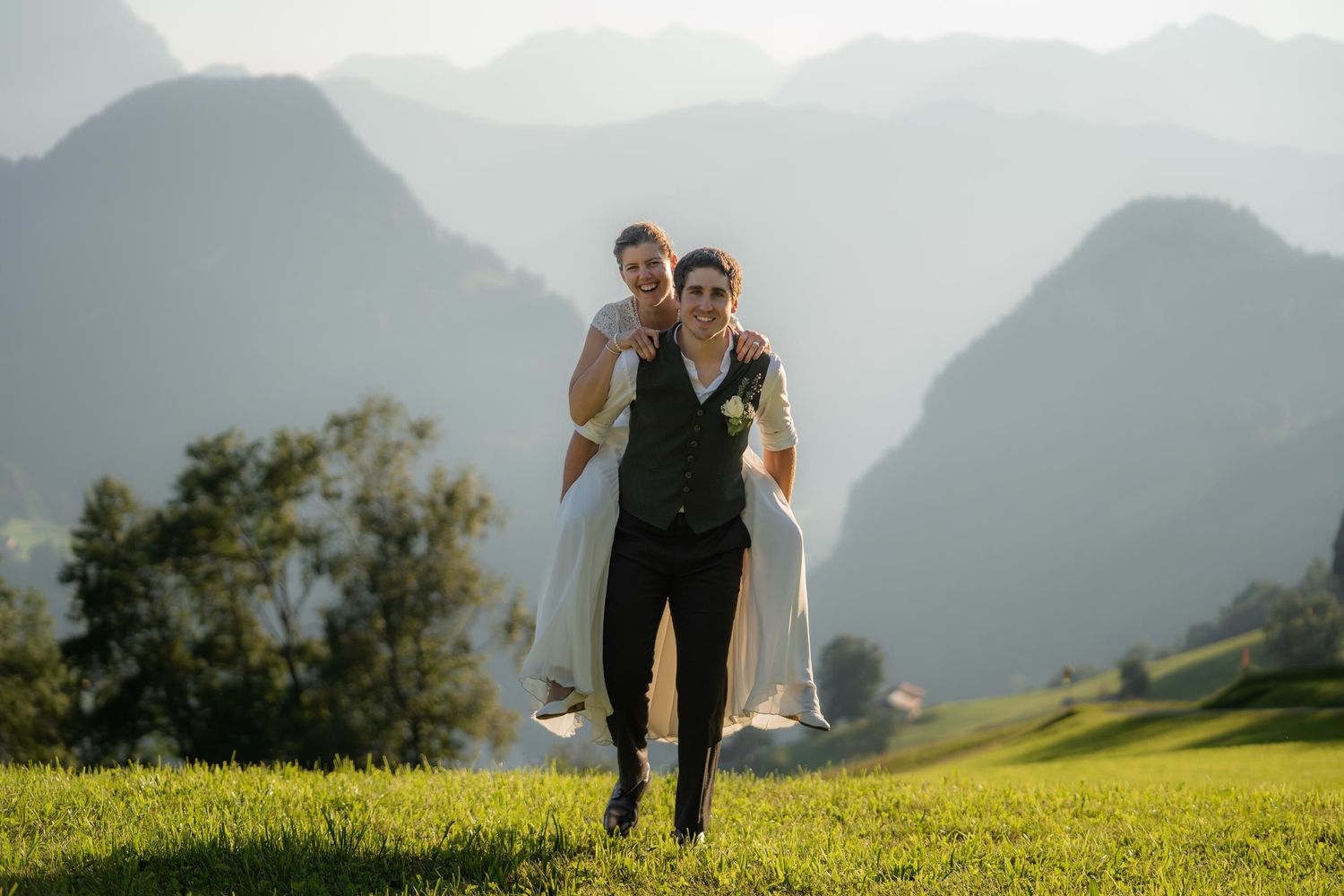 Hochzeitsfotografie: Hochzeitspaar läuft auf einer Wiese – während der Bräutigam die Braut auf den Schultern trägt