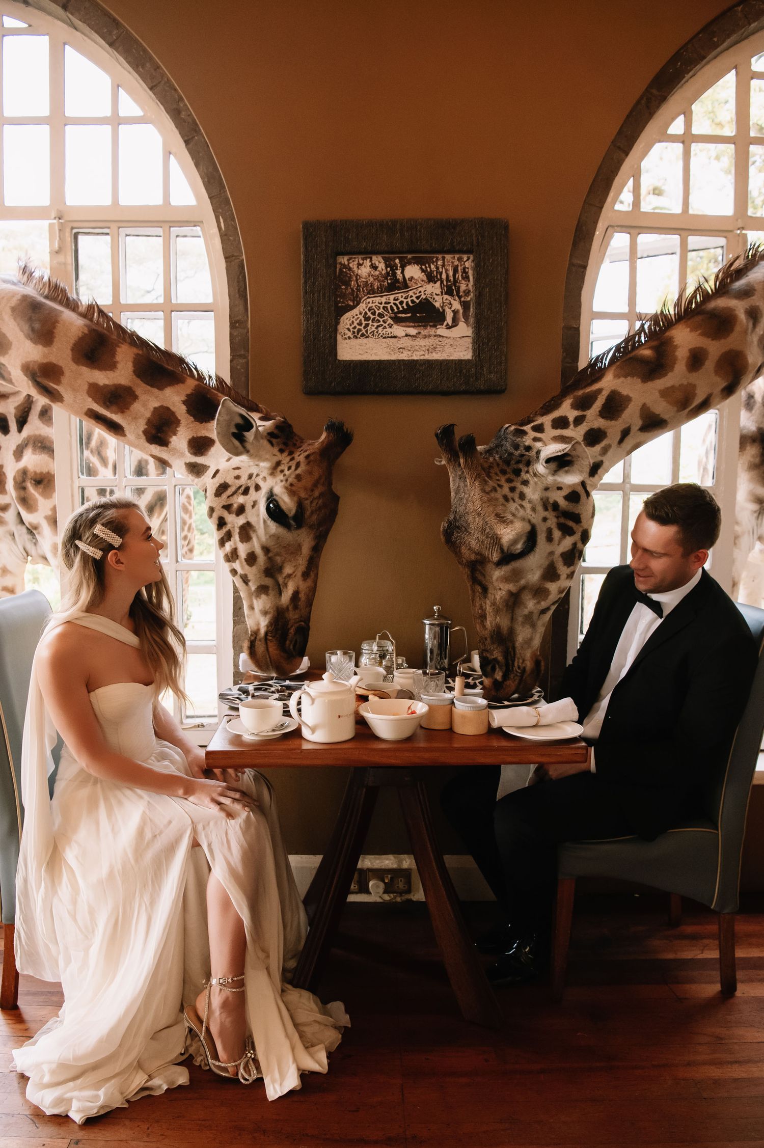 A surreal photo series shows a couple dining with a giraffe in an elegant restaurant setting.