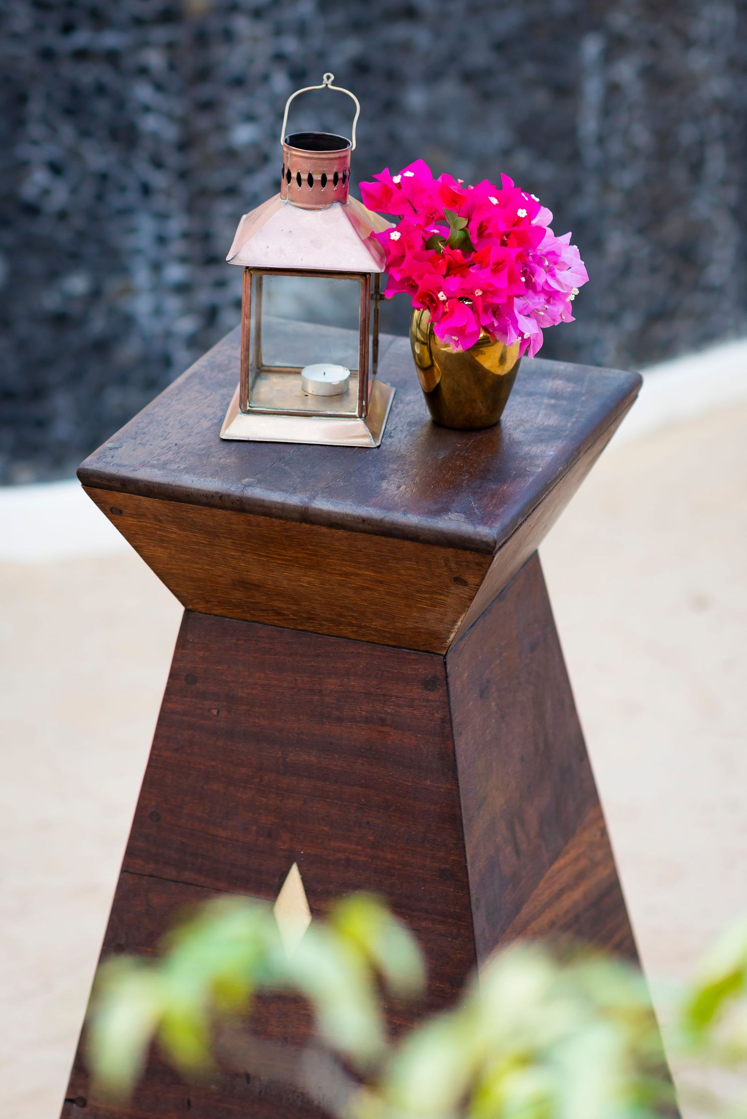 A rustic wooden pedestal displays a pink lantern and bright pink bougainvillea flowers in a small pot.