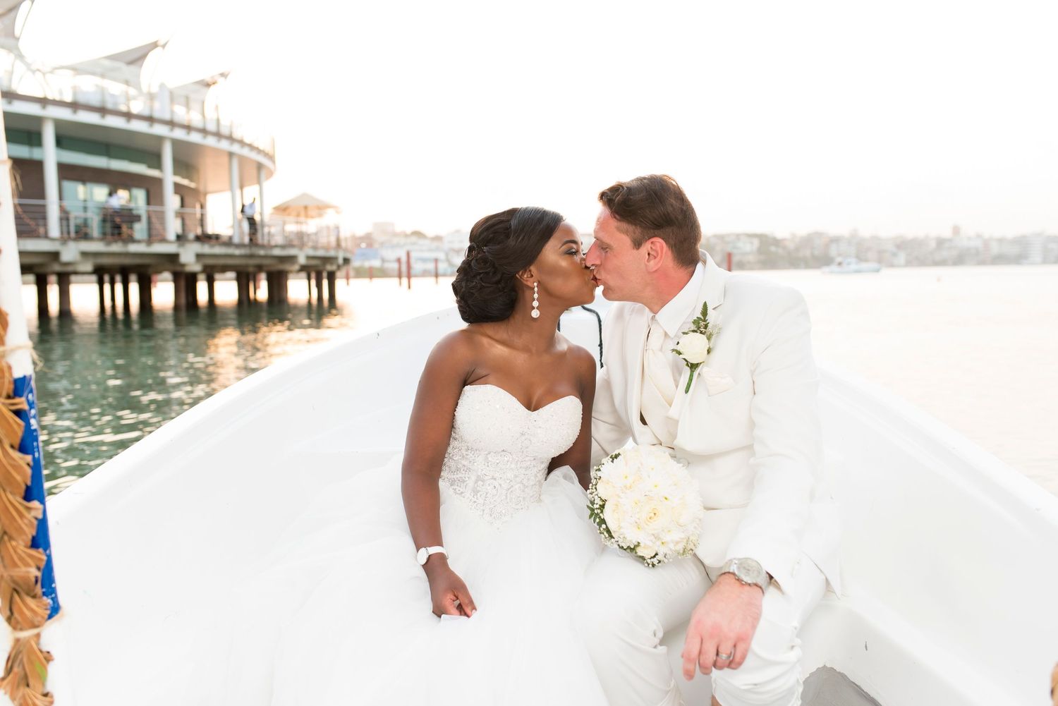 Wedding couple embracing on a white dock by the water during sunset.