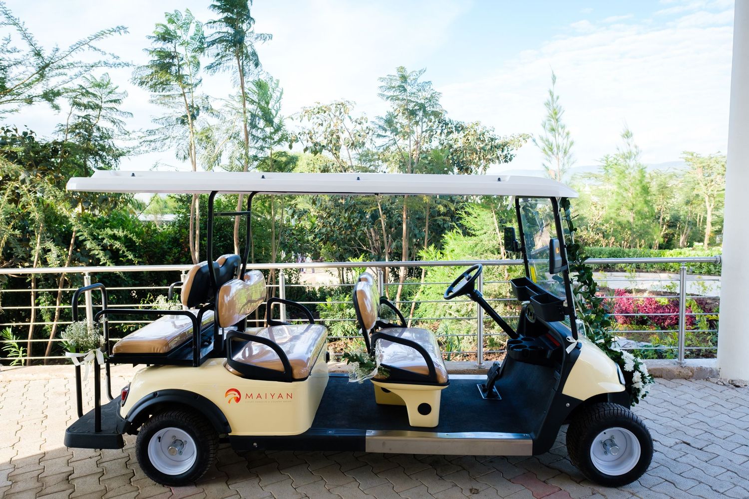 Two beige golf carts parked on a brick paved path with tropical trees and greenery in the background.