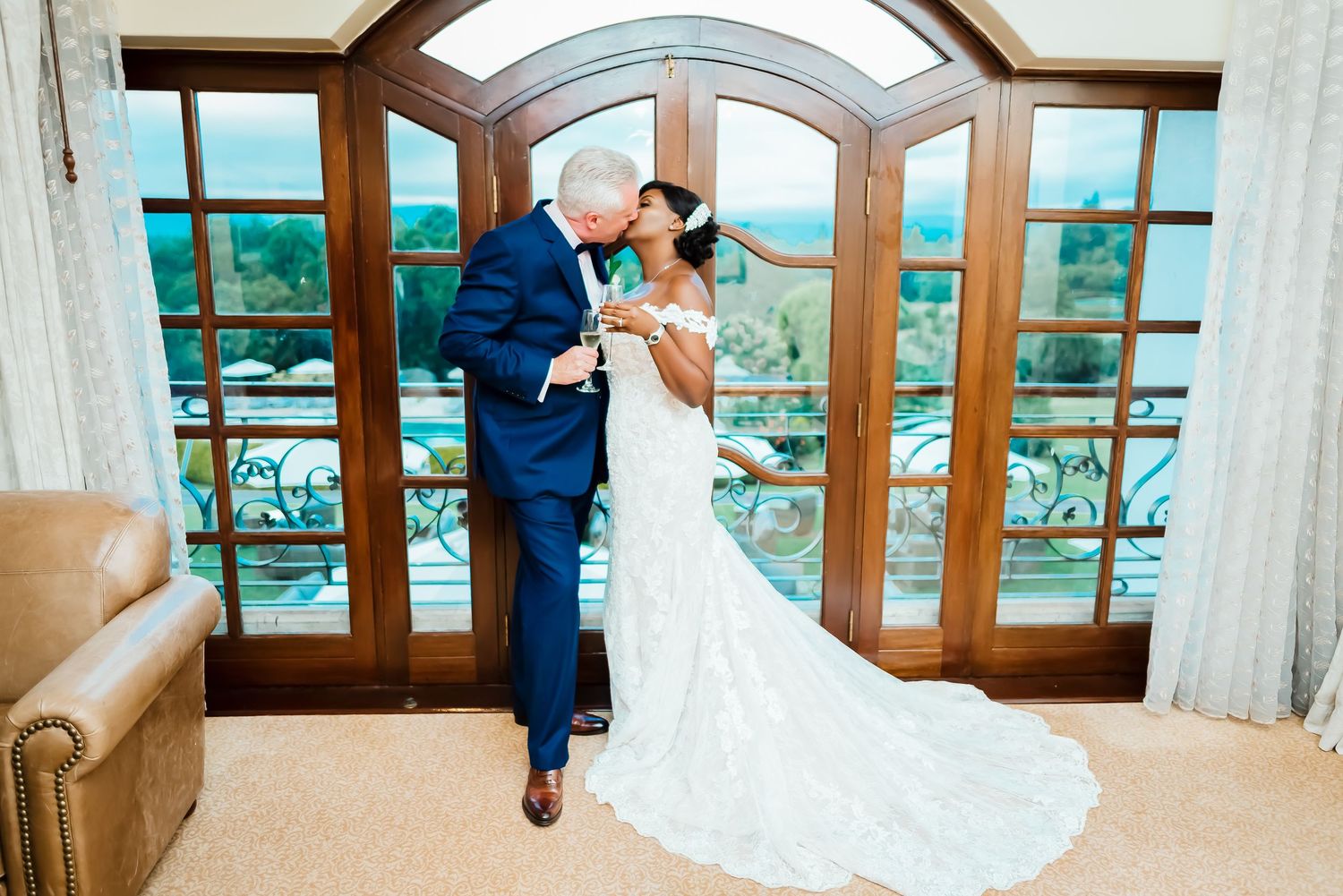Couple shares romantic moment in elegant venue with arched windows overlooking scenic mountain landscape.