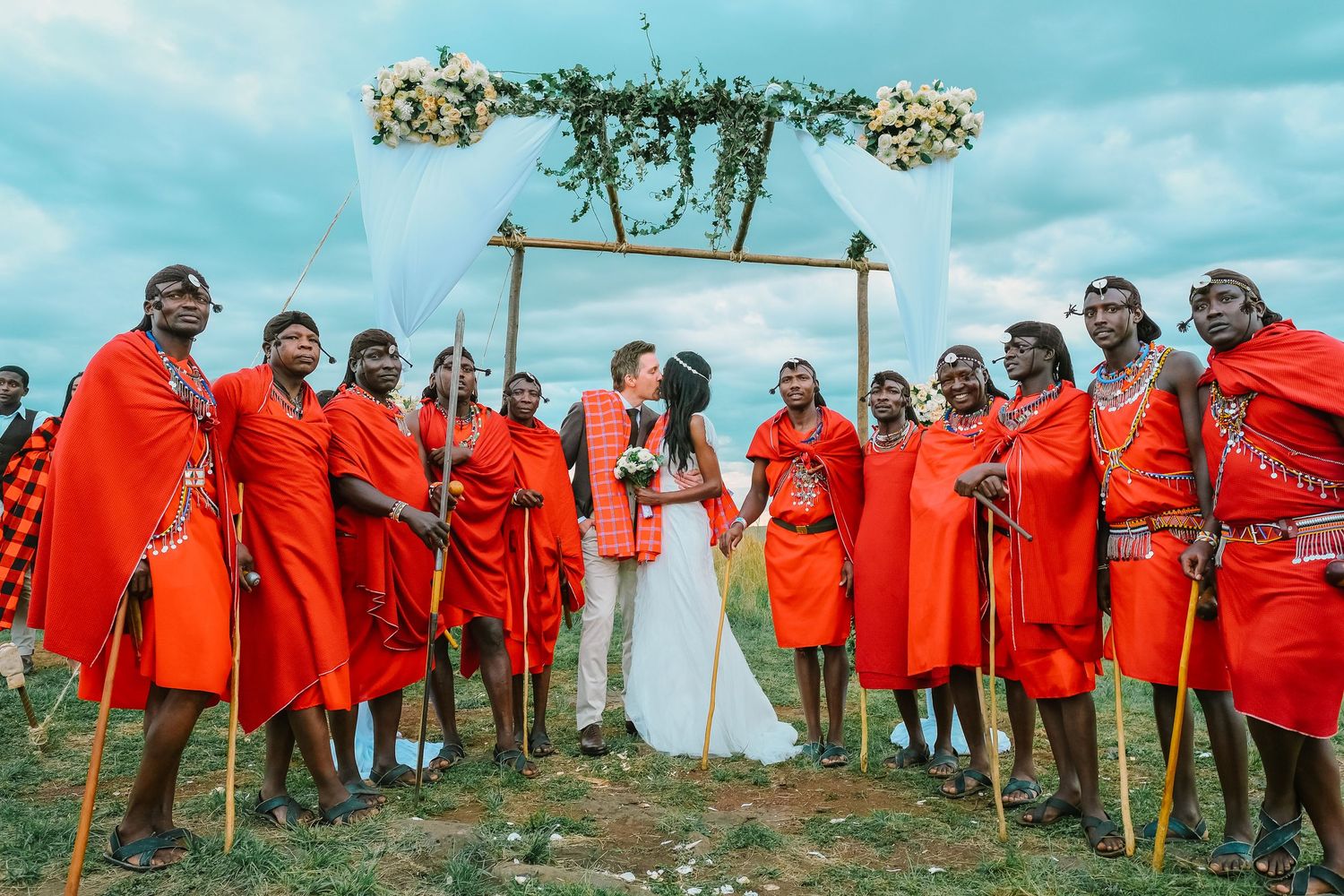 A group of people wearing bright red traditional Maasai robes gather together on a grassy hillside in Kenya.
