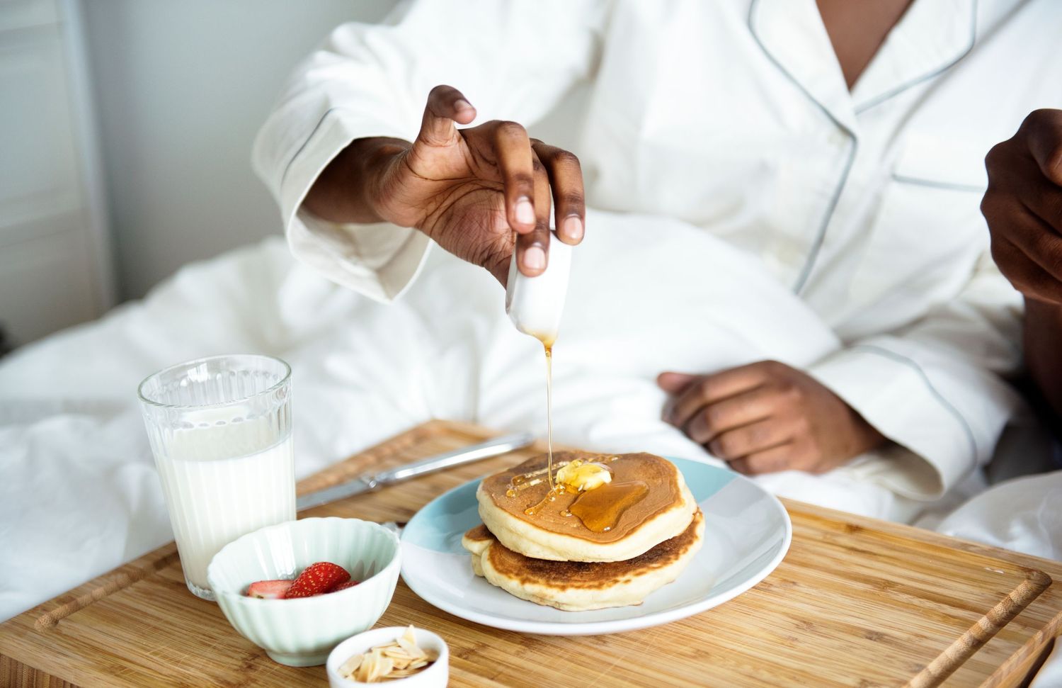 A series of photos showing hands preparing and eating pancakes with syrup and toppings on a wooden table.