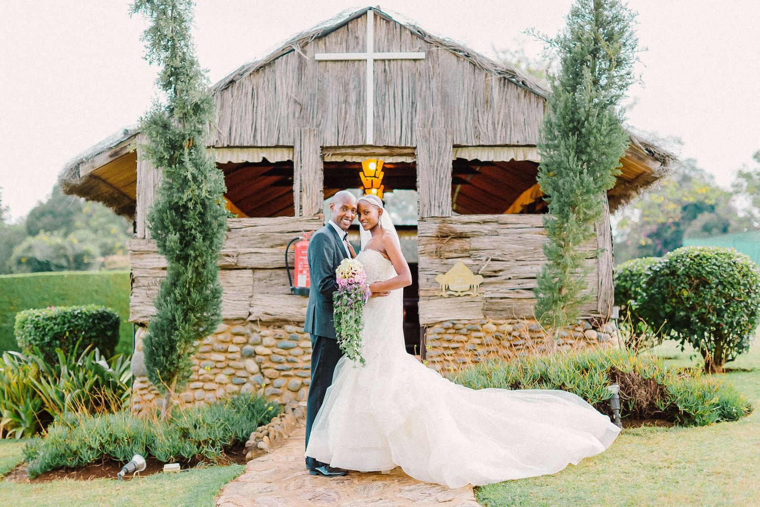 A rustic barn wedding venue with evergreen trees and stone walls creates a romantic countryside setting.