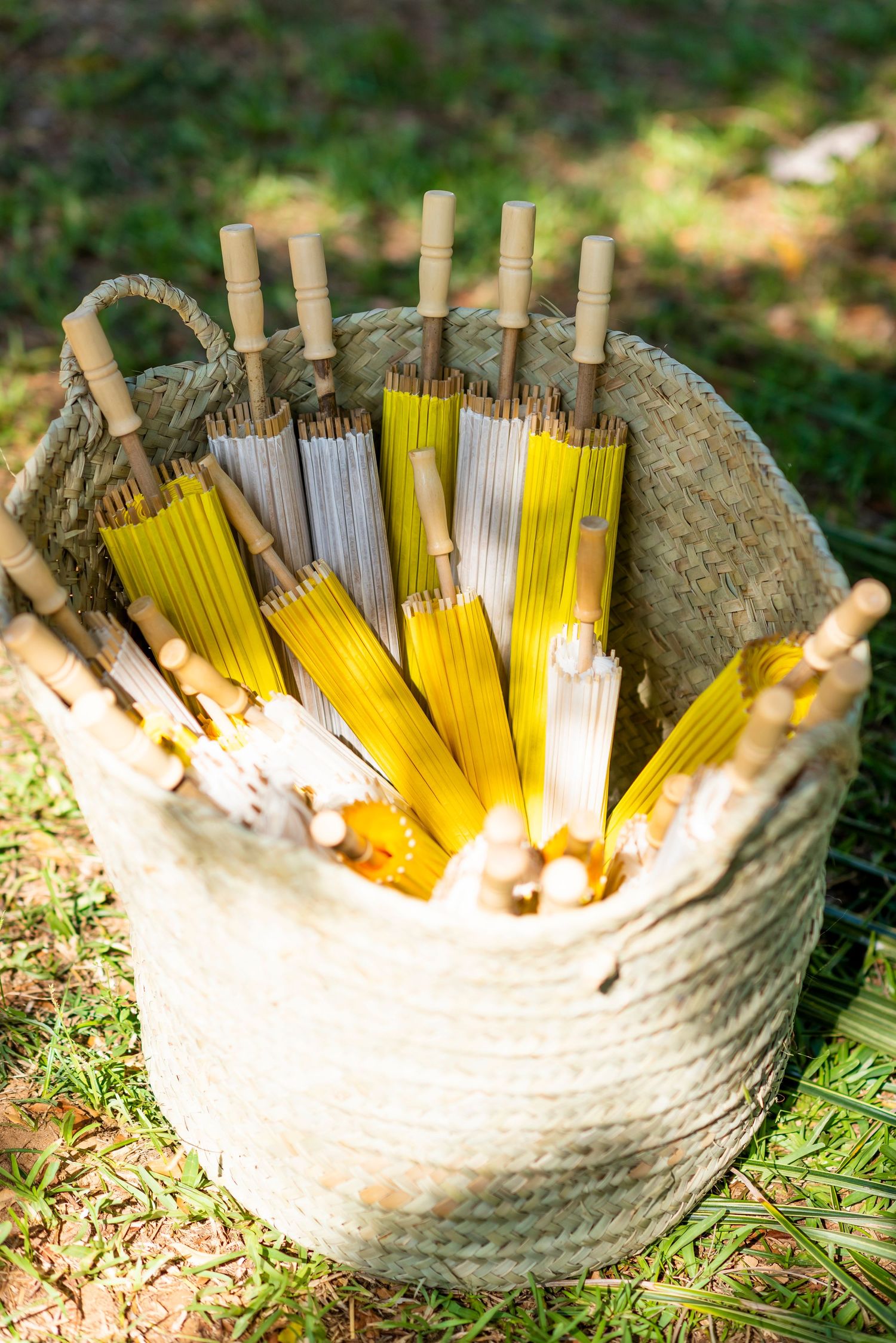 Rustic woven basket filled with yellow and white incense sticks arranged in a fan pattern on grass.
