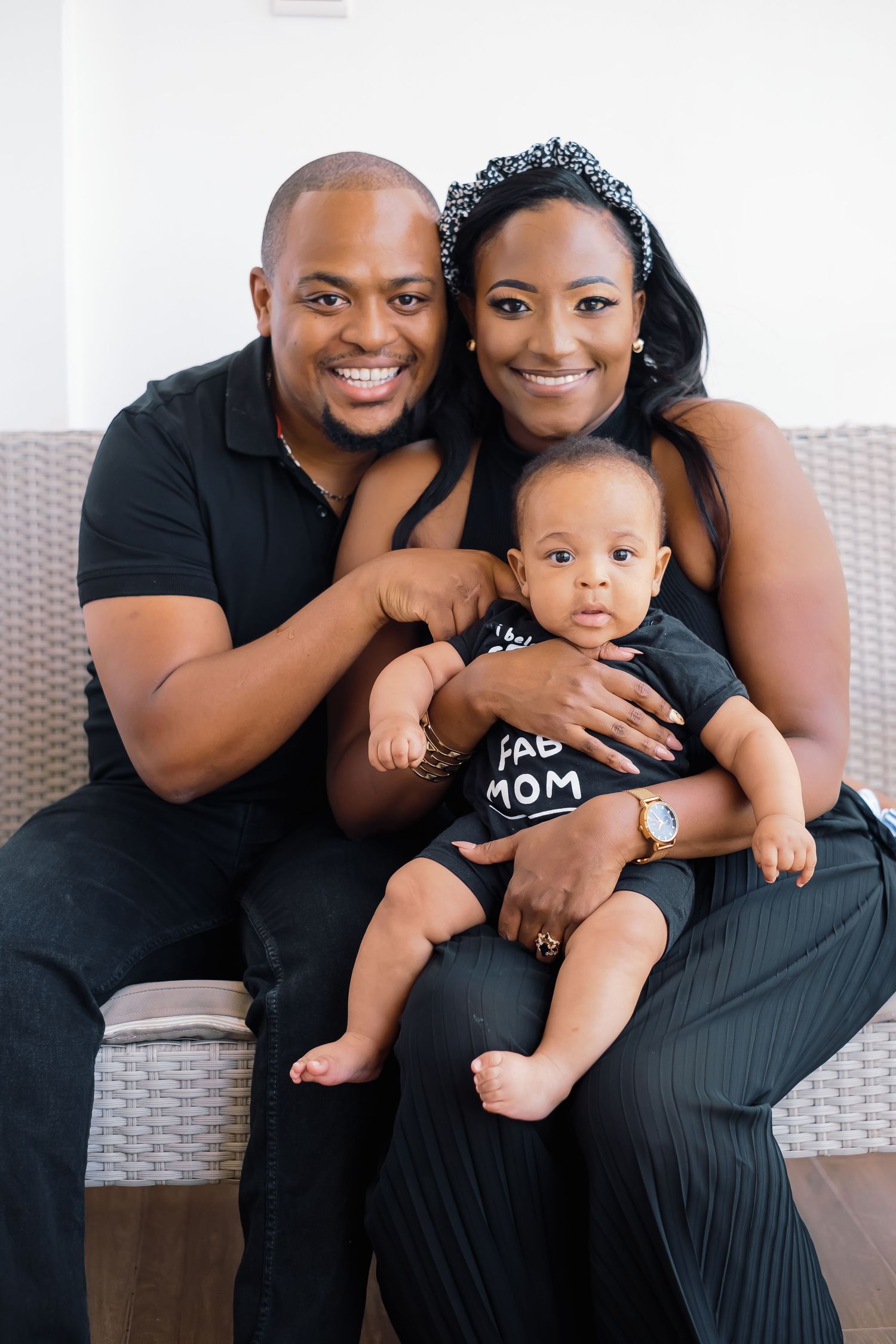 A family wearing black outfits poses together on a grey couch.