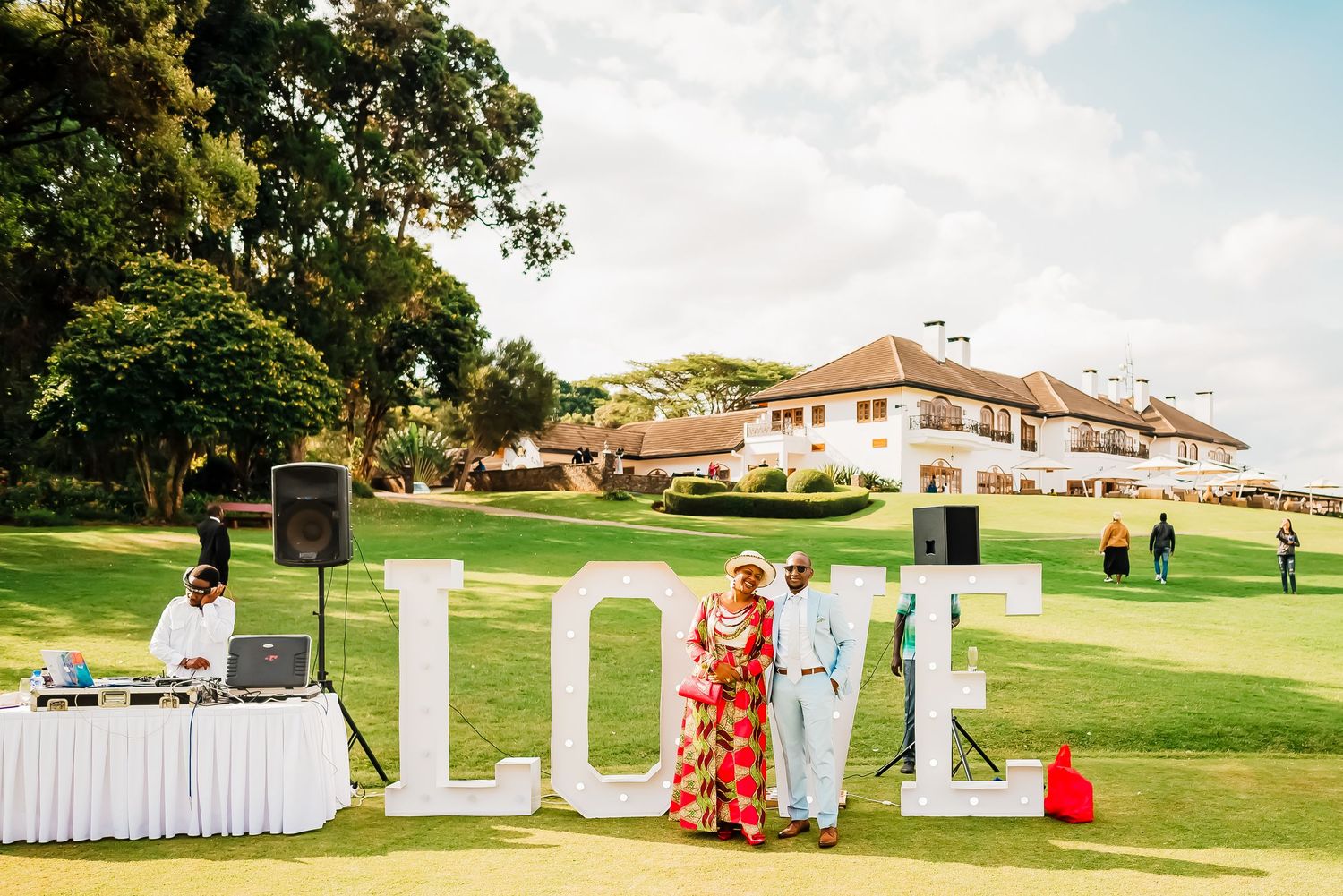 Large white block letters spell out LOVE on a lush green golf course lawn with buildings in the background.