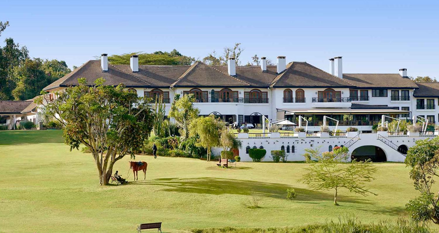 Scenic panoramic view of a golf course with rolling green fairways and palm trees against a bright blue sky.