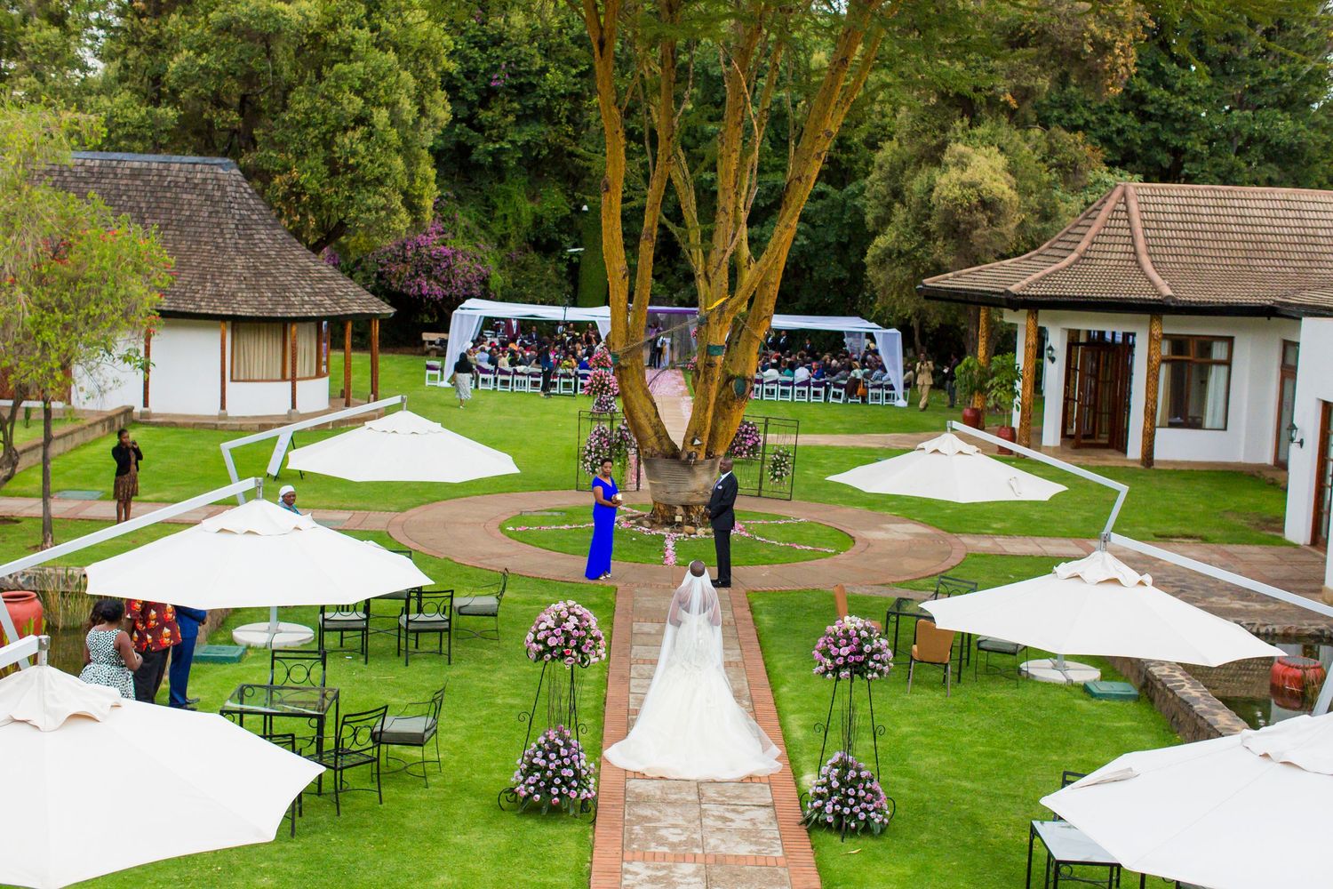 White wedding tents and chairs arranged on a lush green lawn surrounded by trees for an outdoor celebration.
