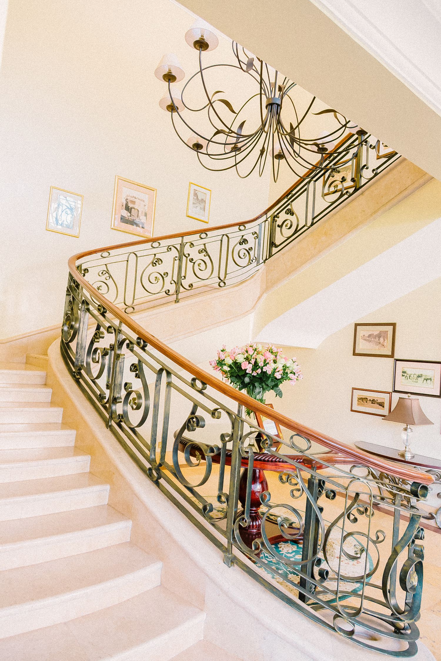 Elegant curved staircase with ornate wrought iron railings and chandelier in a luxury home interior.