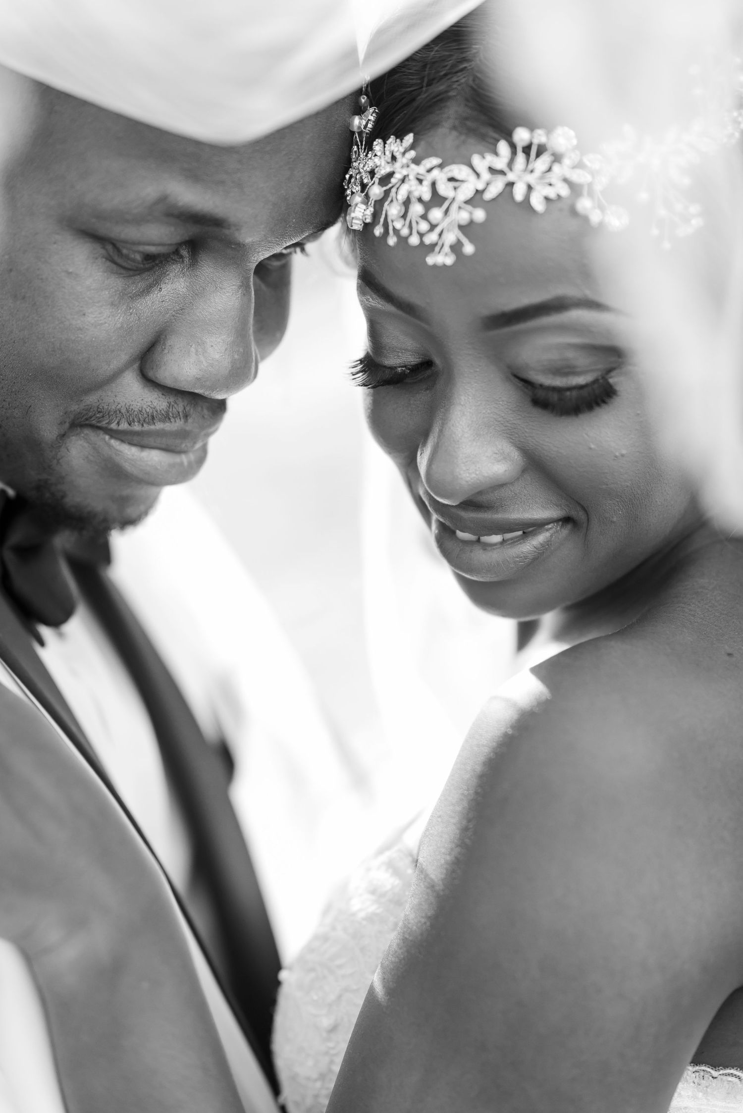 A tender black and white wedding portrait showing an intimate moment between newlyweds with a delicate floral headpiece.