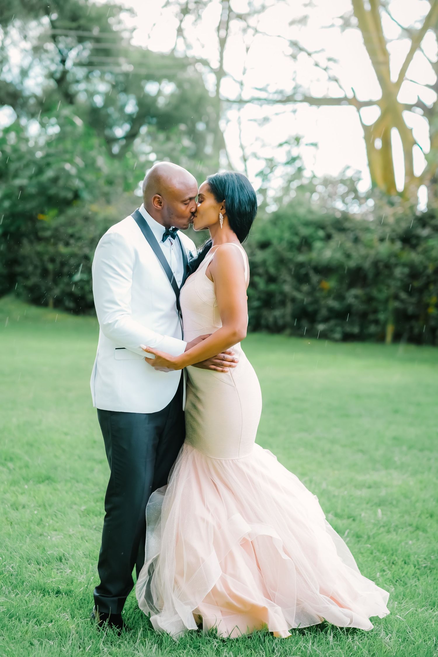 A romantic couple shares a tender kiss in a garden setting while wearing formal wedding attire.