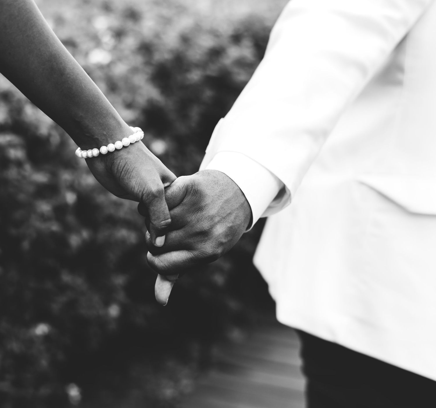 Close-up of hands holding a white wedding dress in an outdoor garden setting.