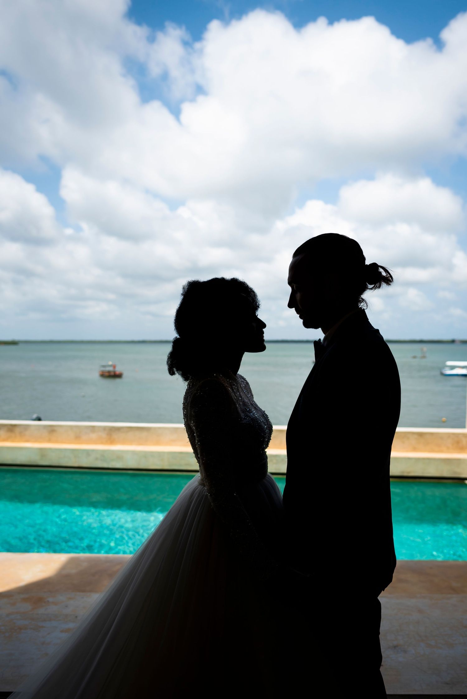 Silhouetted couple against turquoise ocean and cloudy sky background in romantic seaside moment.