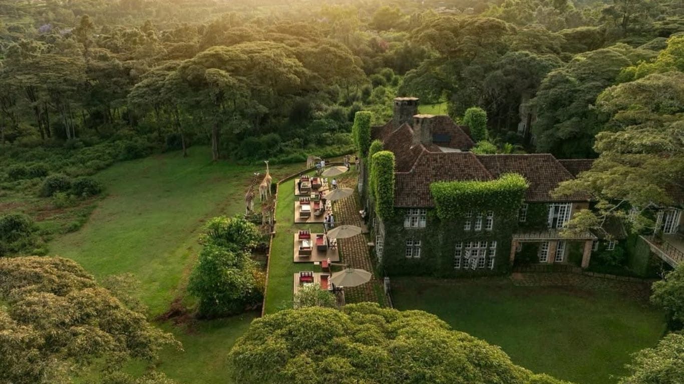 Aerial panoramic view of a lush green countryside estate with Tudor-style architecture and manicured gardens.