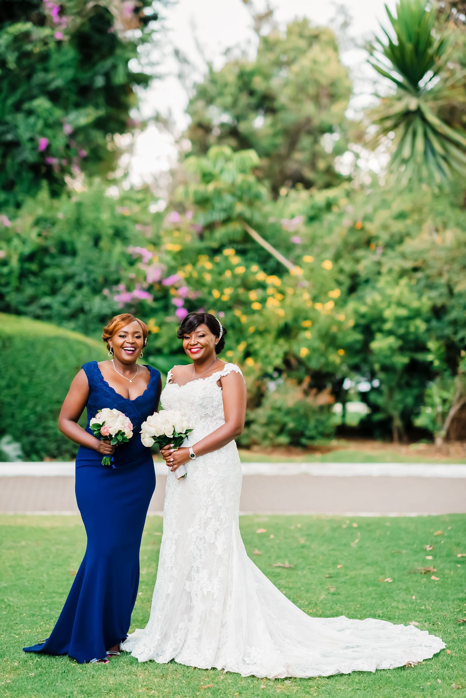 Two people in navy blue and white dresses stand together on a lush green lawn during a wedding celebration.