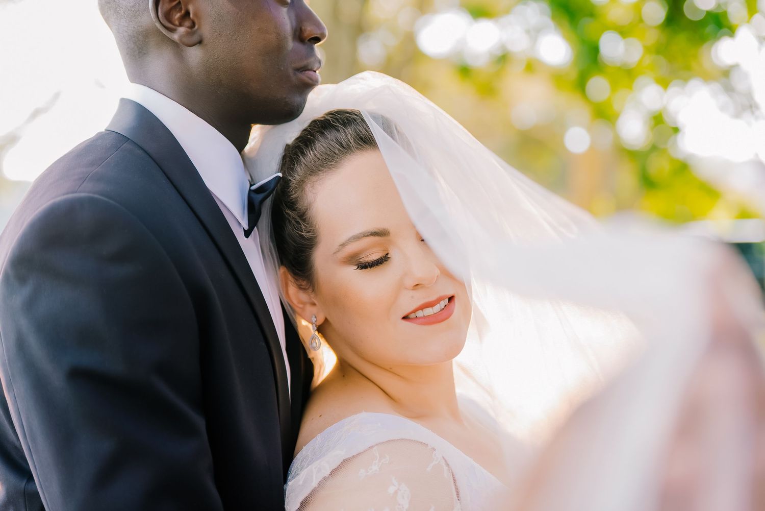 A romantic wedding couple shares an intimate moment outdoors under natural lighting.