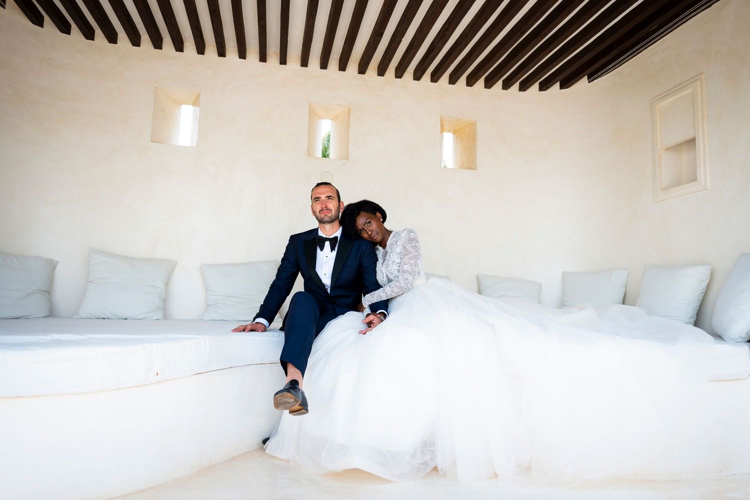 Two people sit in a bright white room with modern pendant lights and black striped ceiling details.