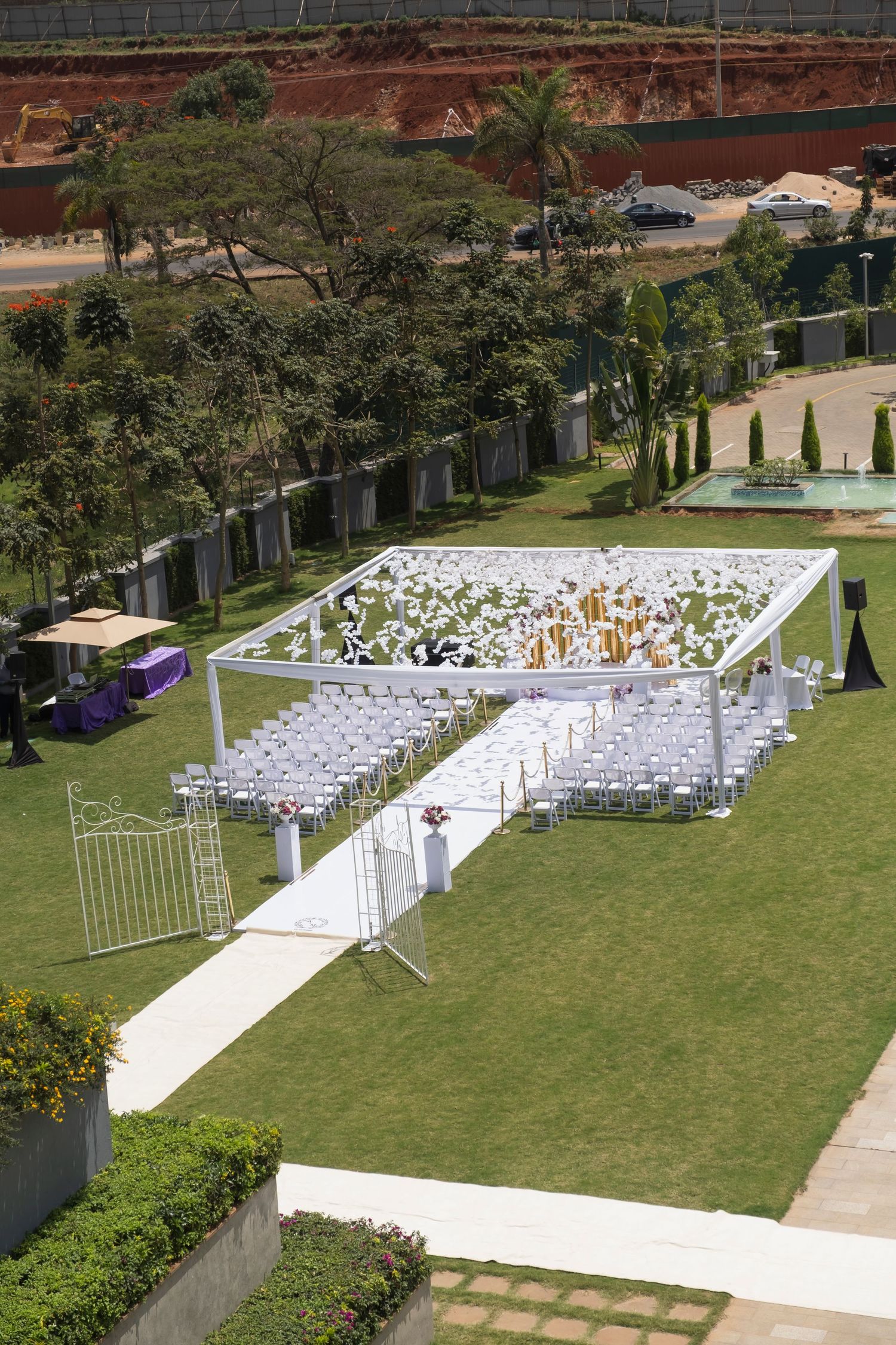 Outdoor wedding ceremony setup with white chairs and archway arranged on a manicured lawn surrounded by tropical landscaping.