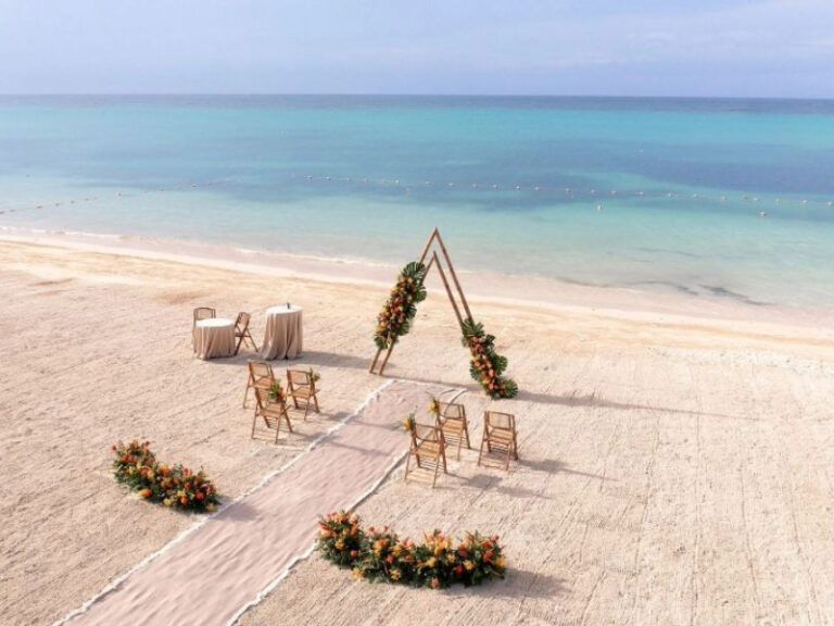 Beach chairs arranged in a curved line on white sand with turquoise ocean waters and clear blue sky in the background.