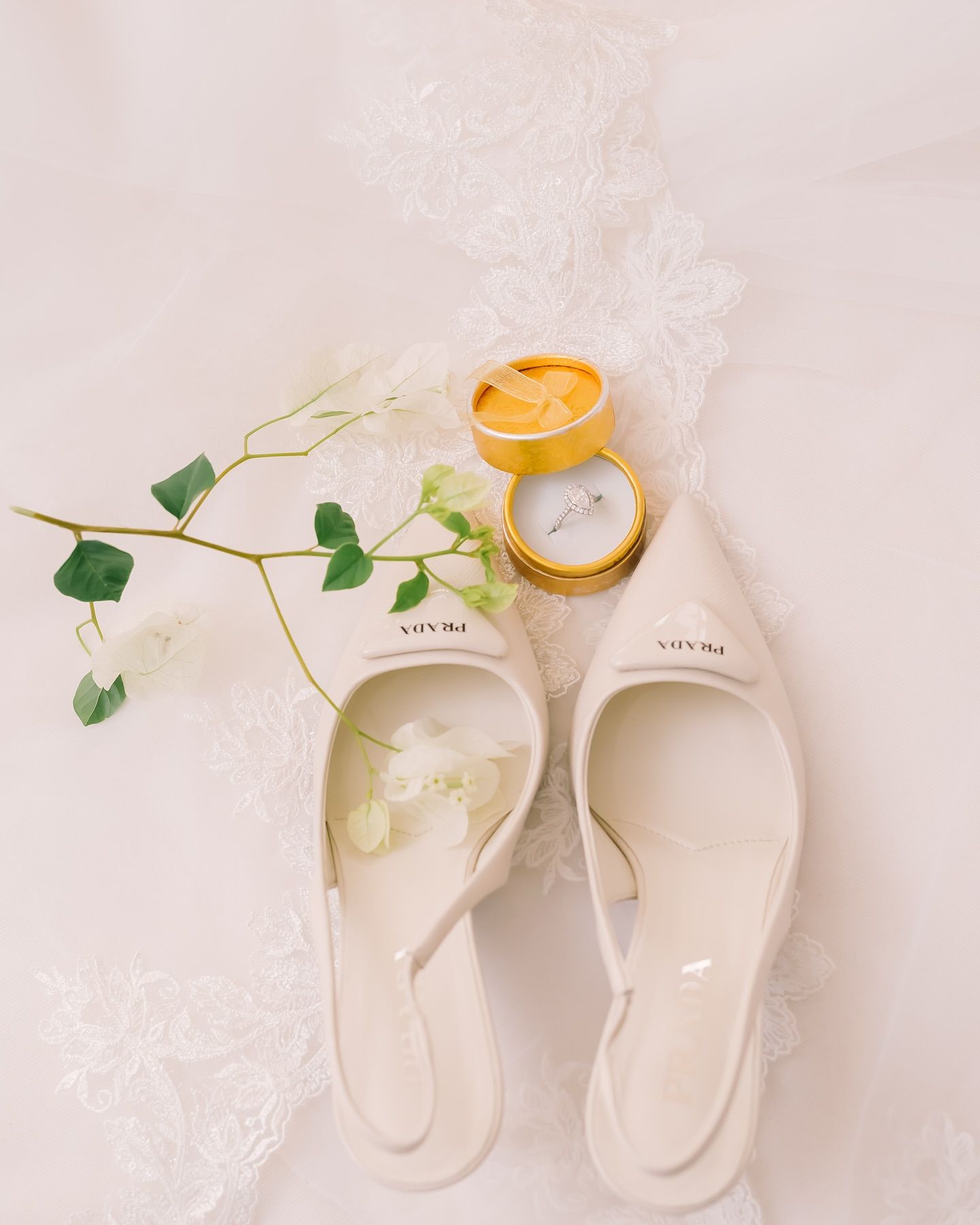 White bridal flats with wedding rings and delicate green vine arranged on lace background in elegant flat lay composition.