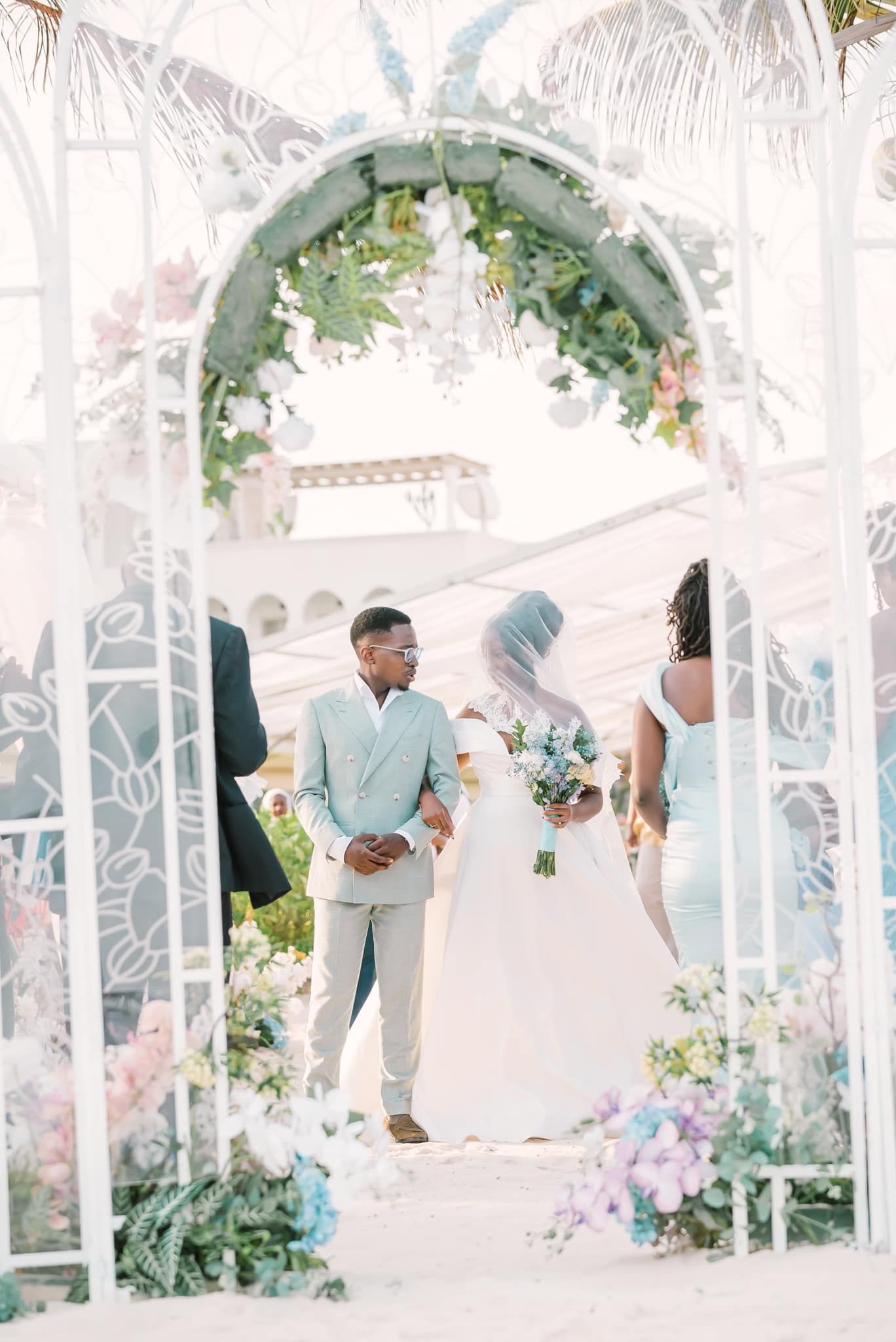 Elegant outdoor wedding ceremony under white gazebo with floral decorations and soft pastel color scheme.