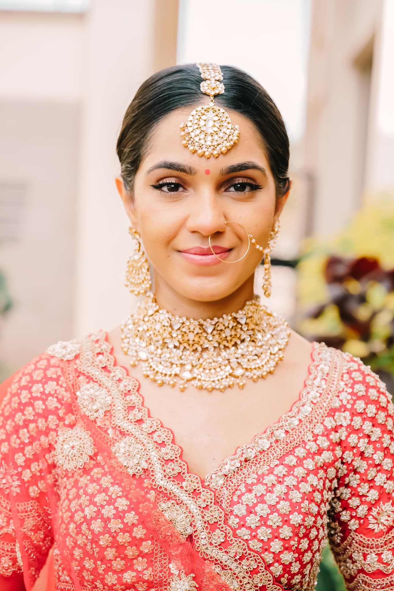Close-up details of traditional Indian bridal jewelry and coral pink lehenga with intricate gold embroidery.